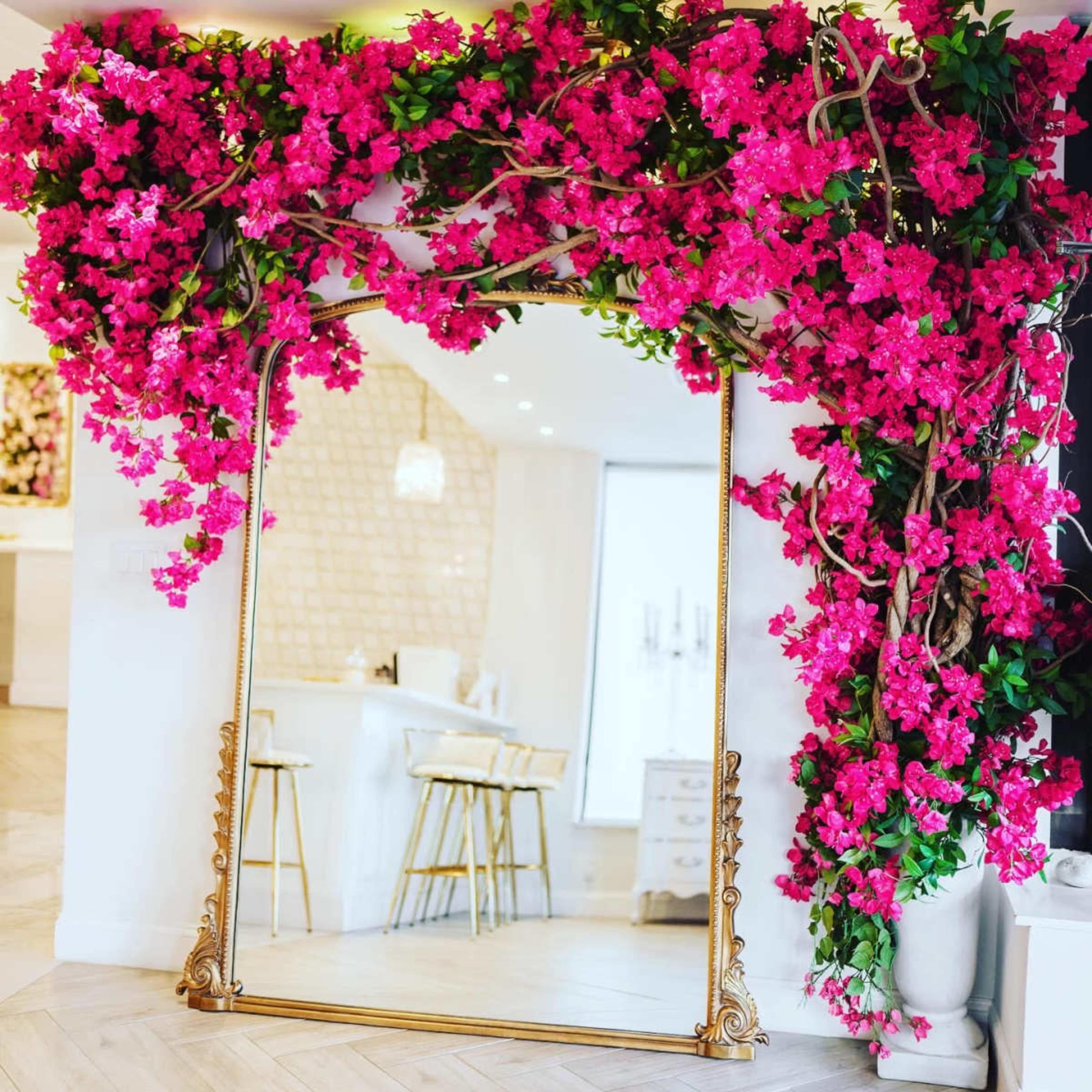 A large, ornate golden mirror is framed by vibrant pink bougainvillea flowers.