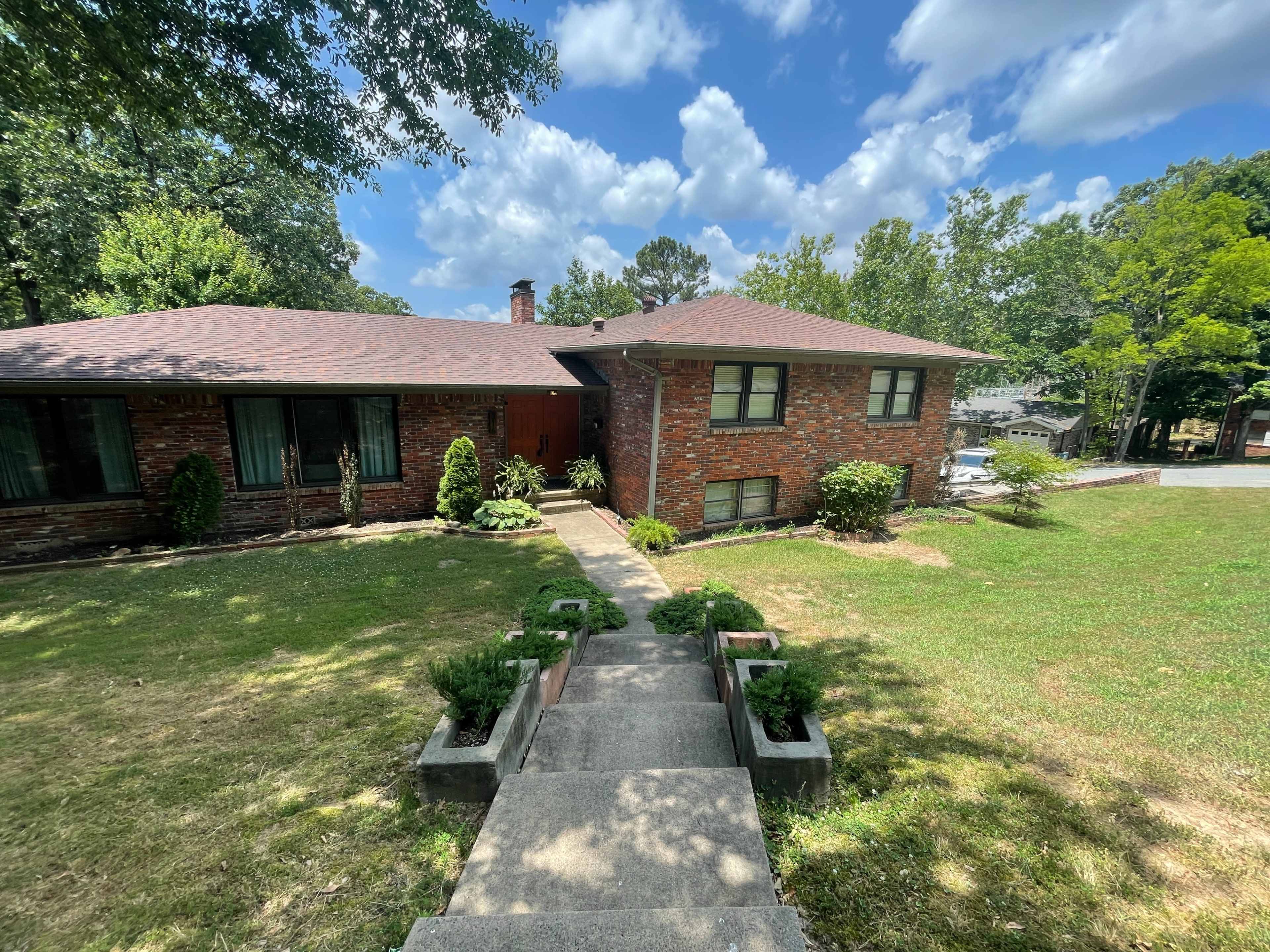 A brick ranch-style house with a landscaped front yard is shown under a partly cloudy sky.