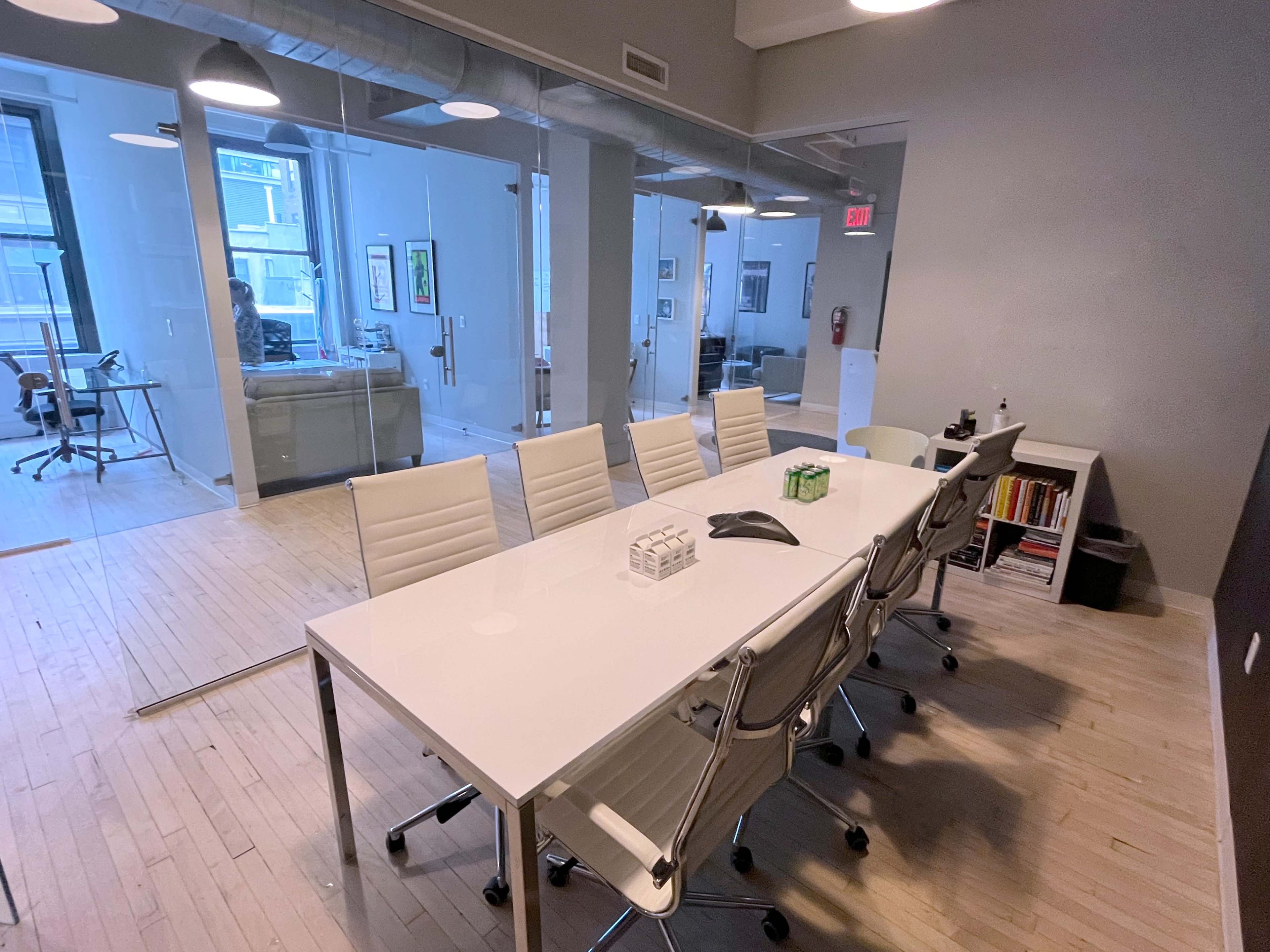 A modern conference room features a long white table surrounded by sleek chairs, adjacent to a glass-walled office space.