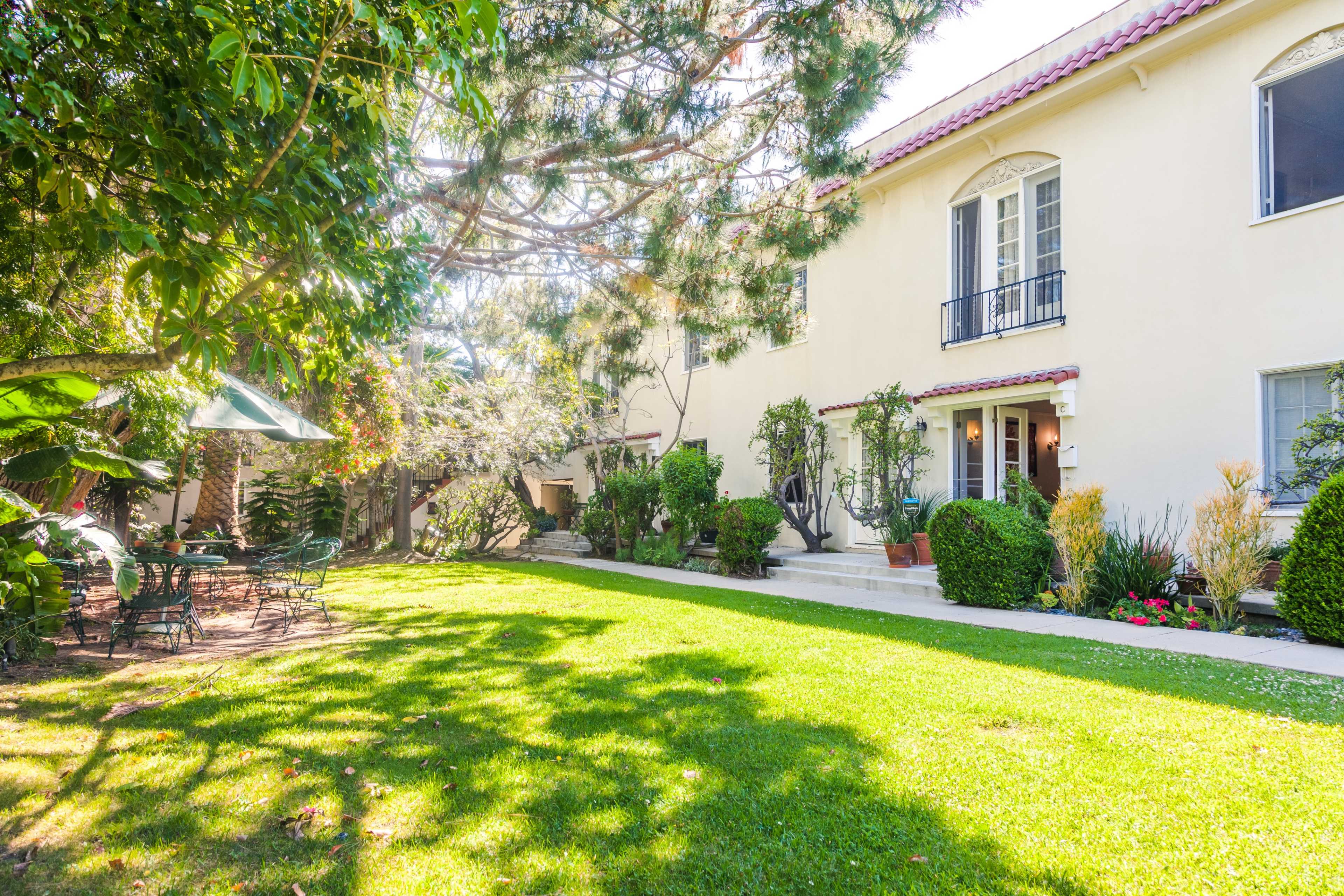 A well-maintained two-story building is set in a lush green garden with various shrubs and trees.