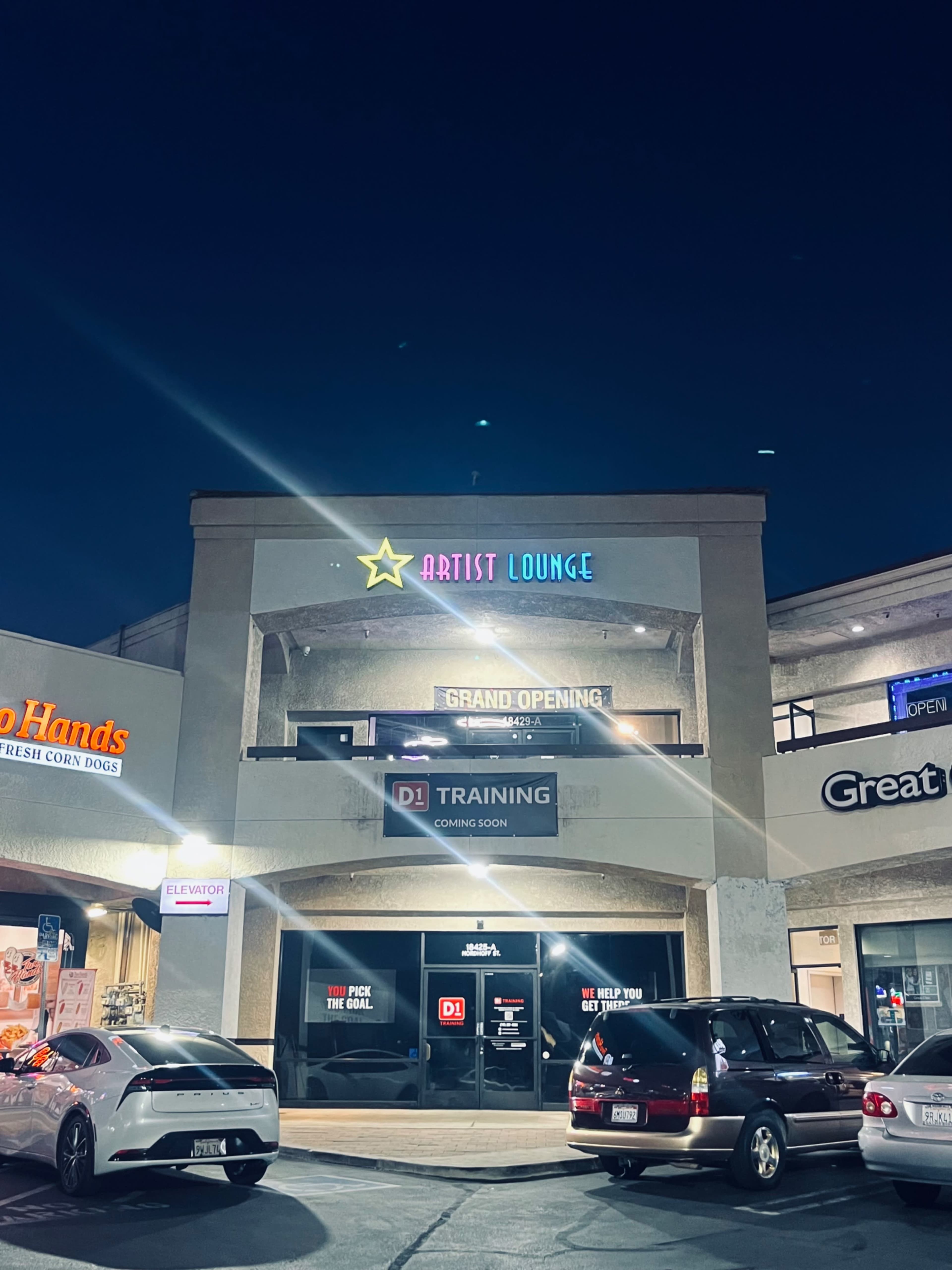 The image shows a two-story commercial building at night with a sign for "Artist Lounge" and a banner for "DJ Training" indicating a grand opening.