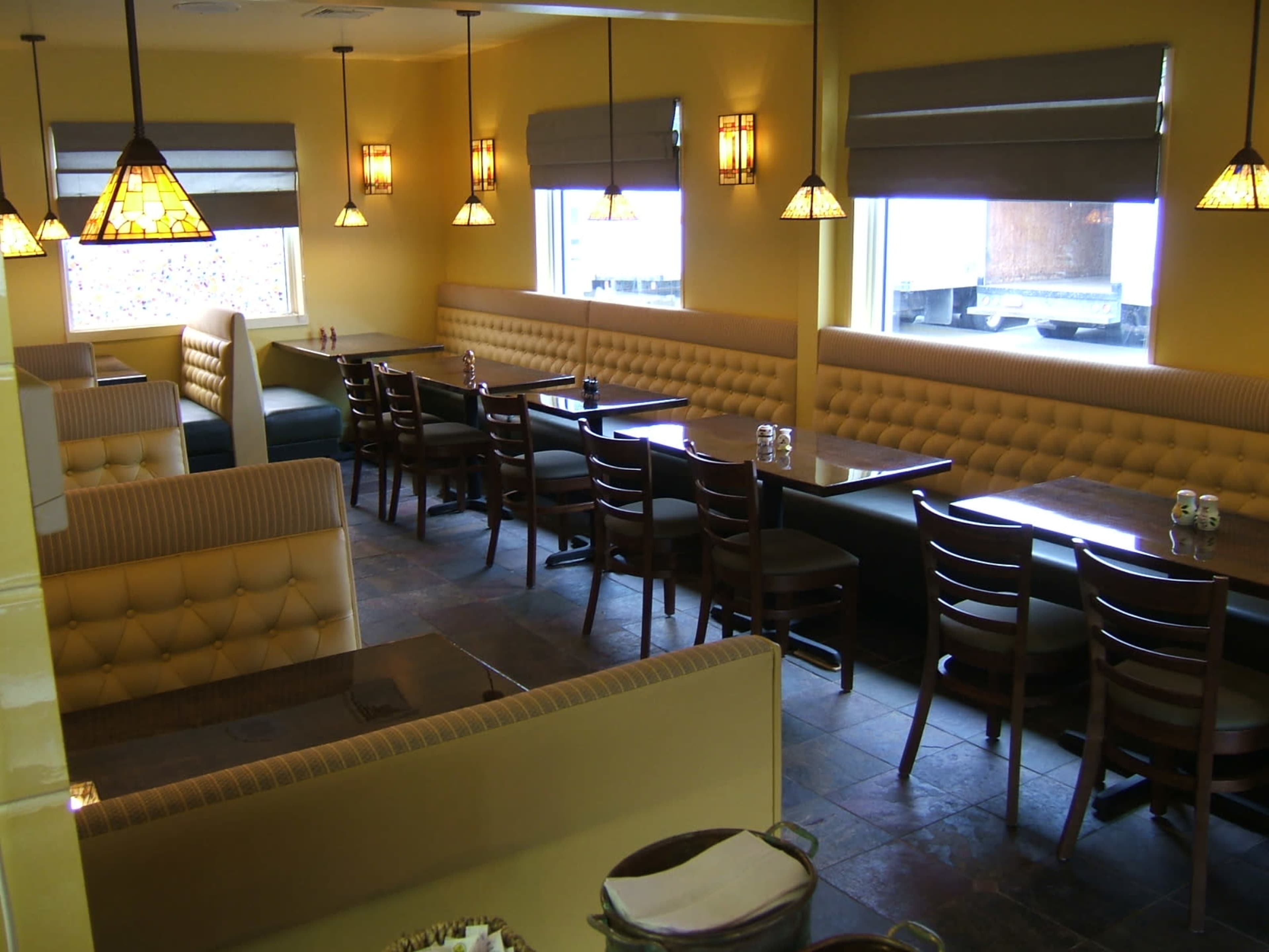 A restaurant interior featuring yellow walls, booth seating, and wooden tables arranged under pendant lighting.