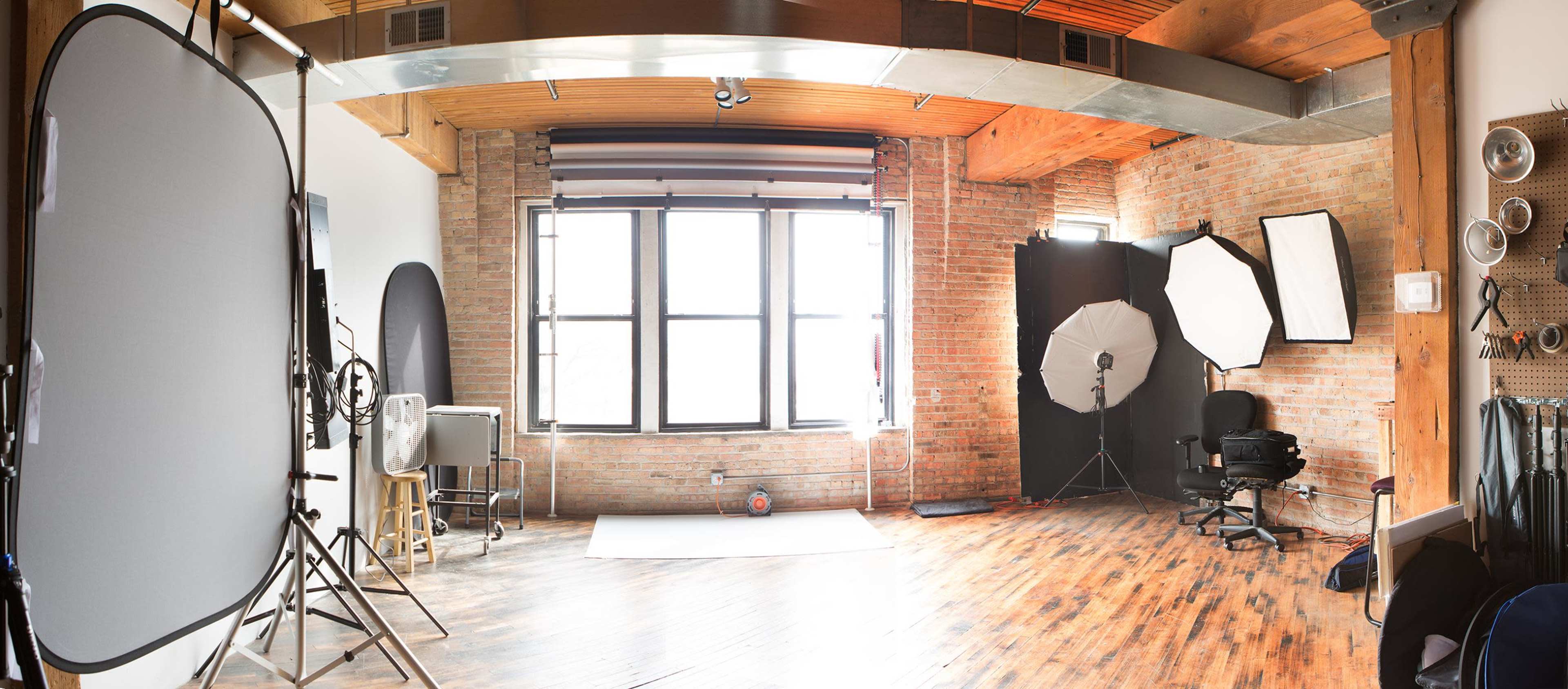 A photography studio with various lighting equipment, a backdrop, and large windows letting in natural light.