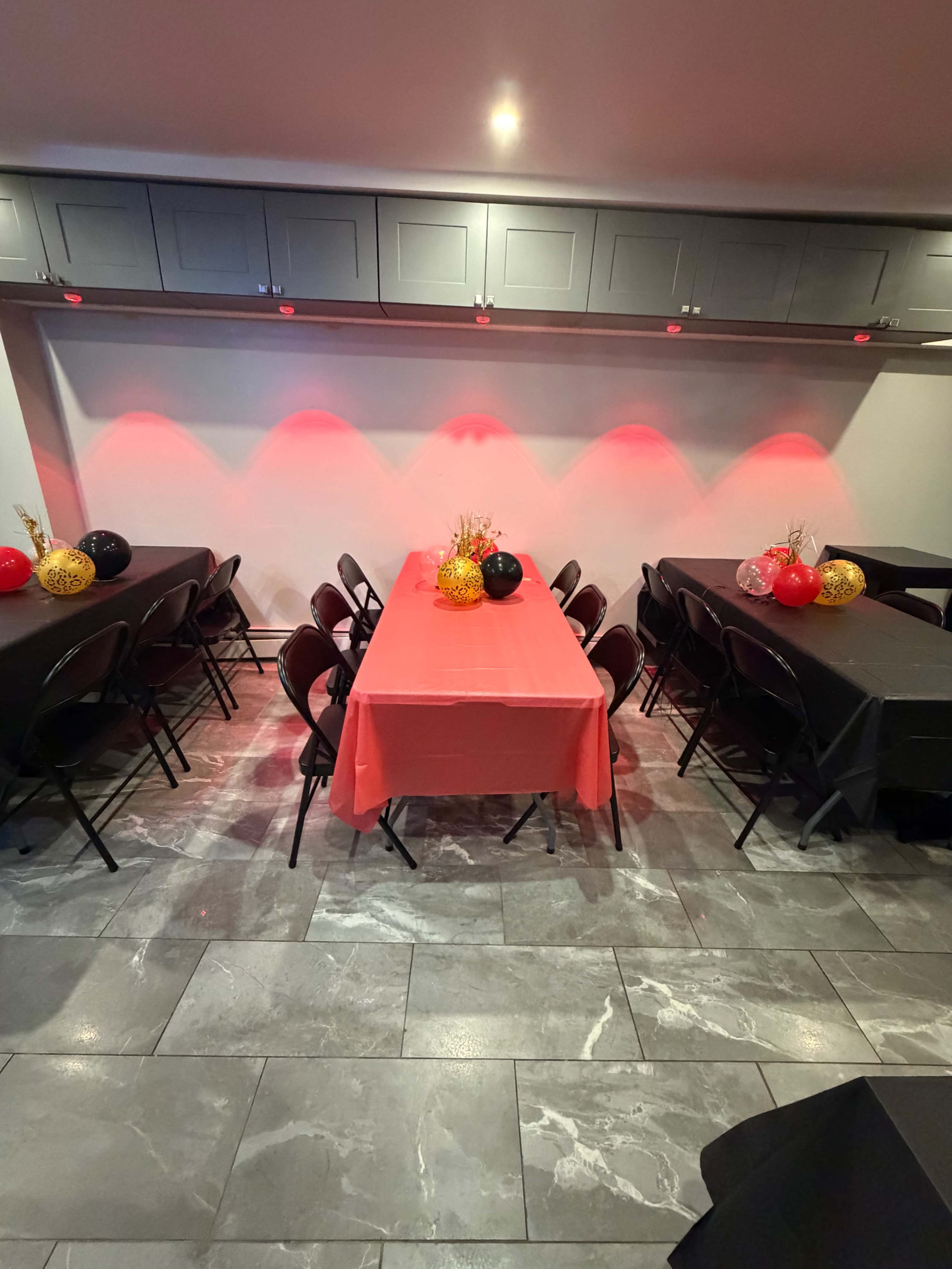 The image shows a party setup with black and red tables decorated with balloons and centerpieces in a room with dim lighting.