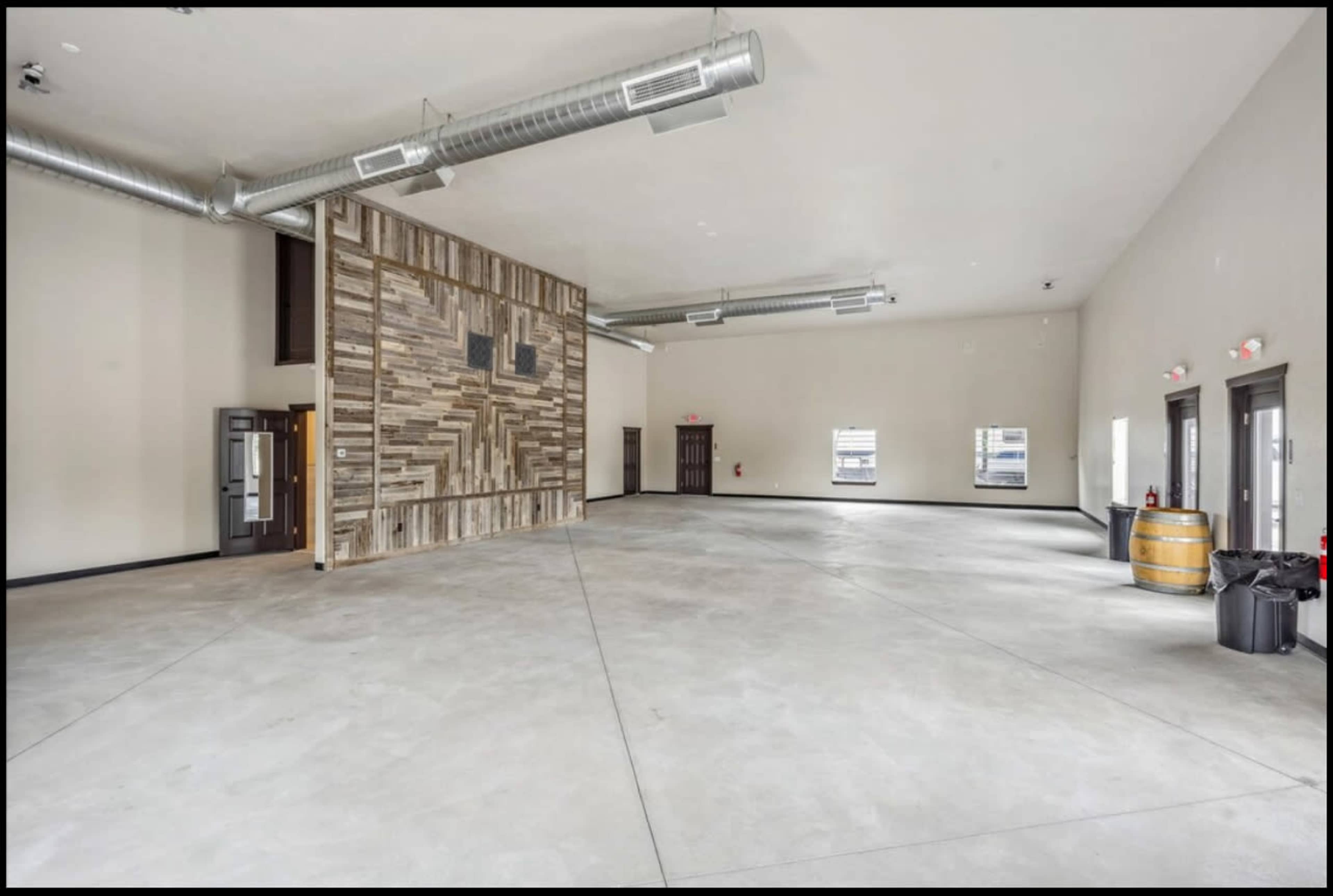 The image shows a spacious, empty room with a wooden accent wall and large, industrial-style ventilation pipes on the ceiling.