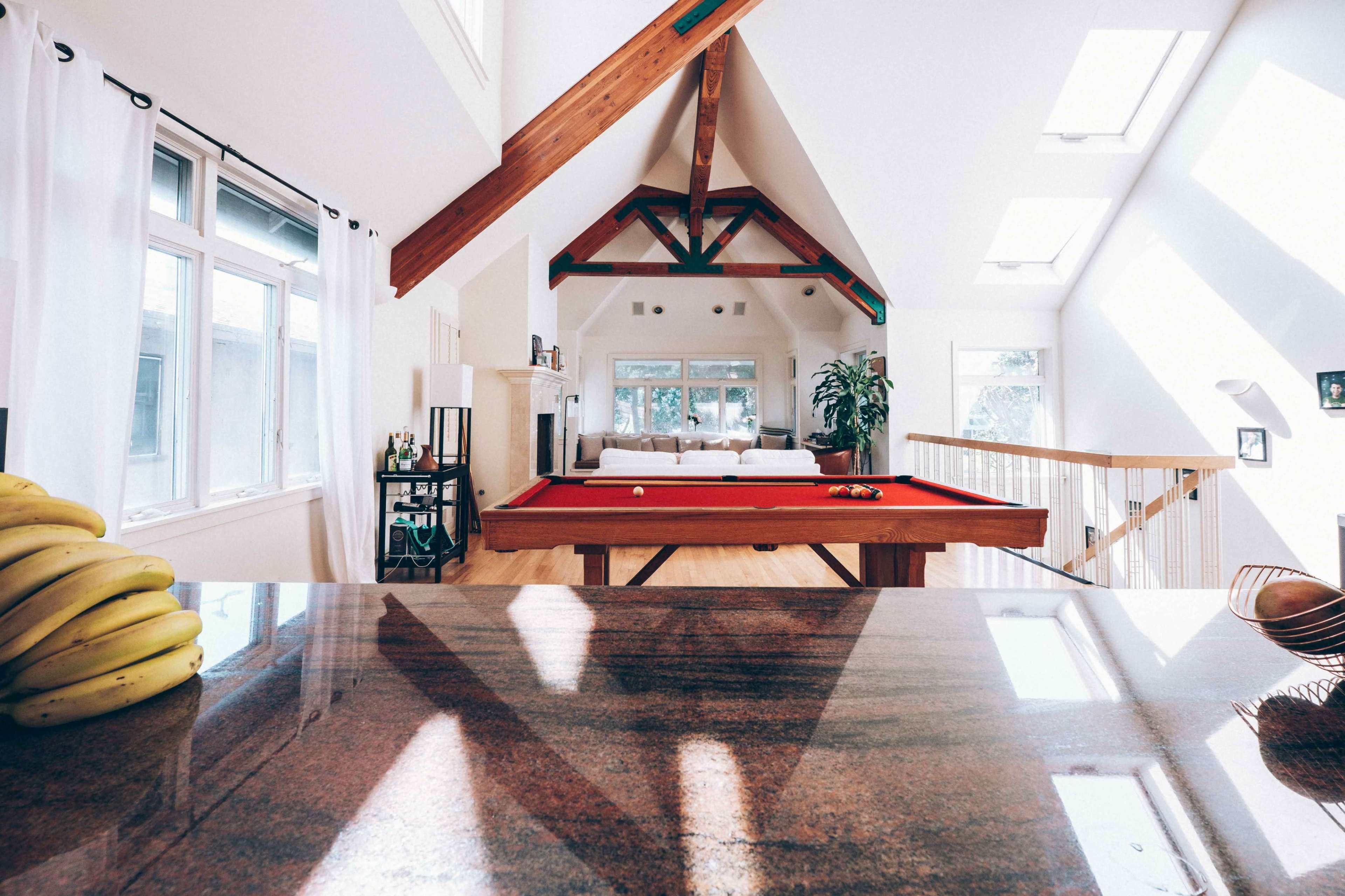 A spacious living area features a billiard table, large windows, and wooden beams in the ceiling.