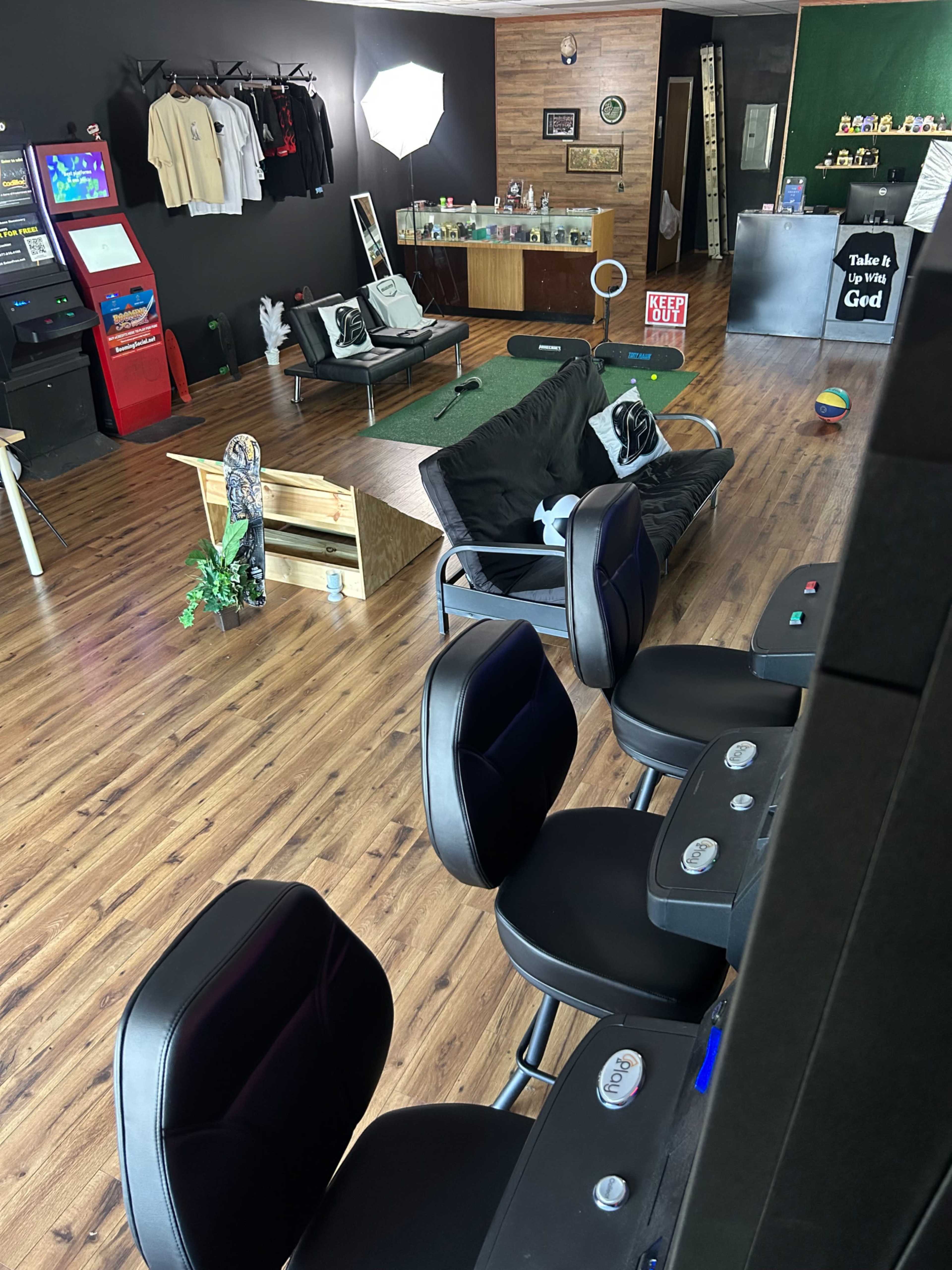 The image shows a modern lounge area with black walls, various seating options, a small putting green, and a display of merchandise on a counter.