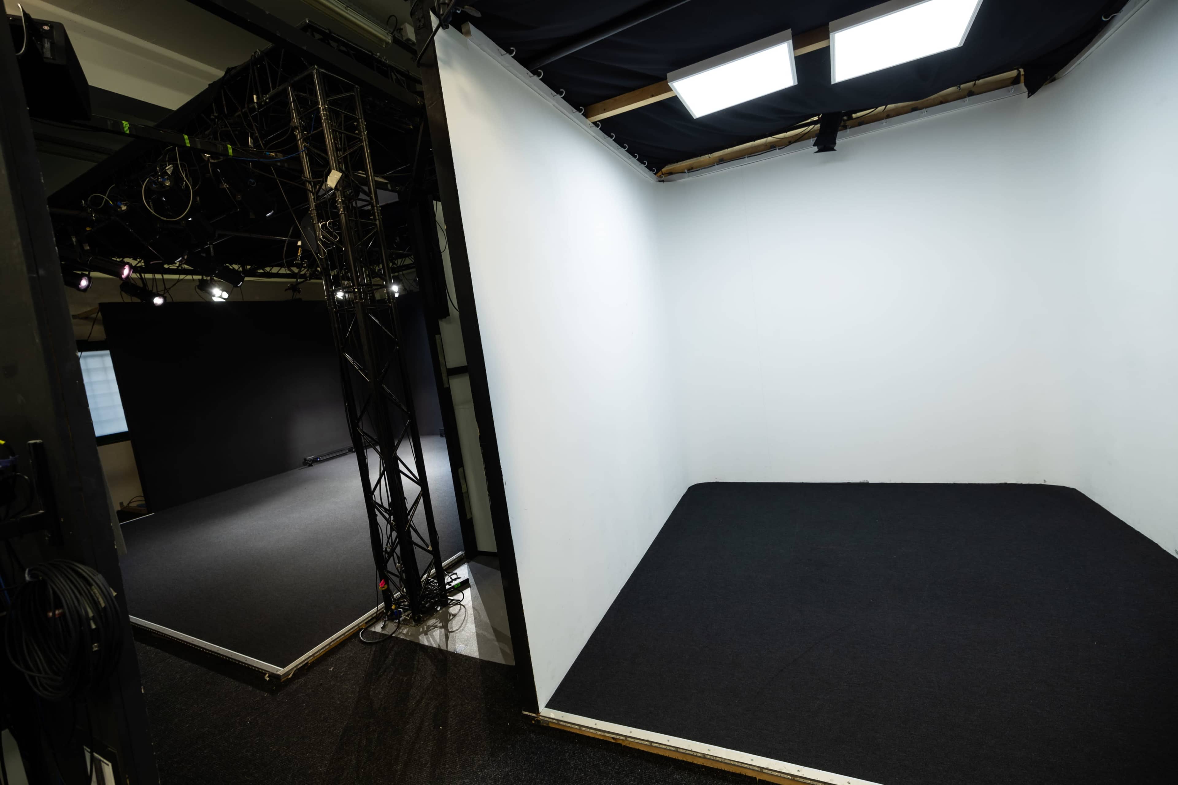 A spacious studio with two separate areas, one featuring a black floor and the other a white backdrop.