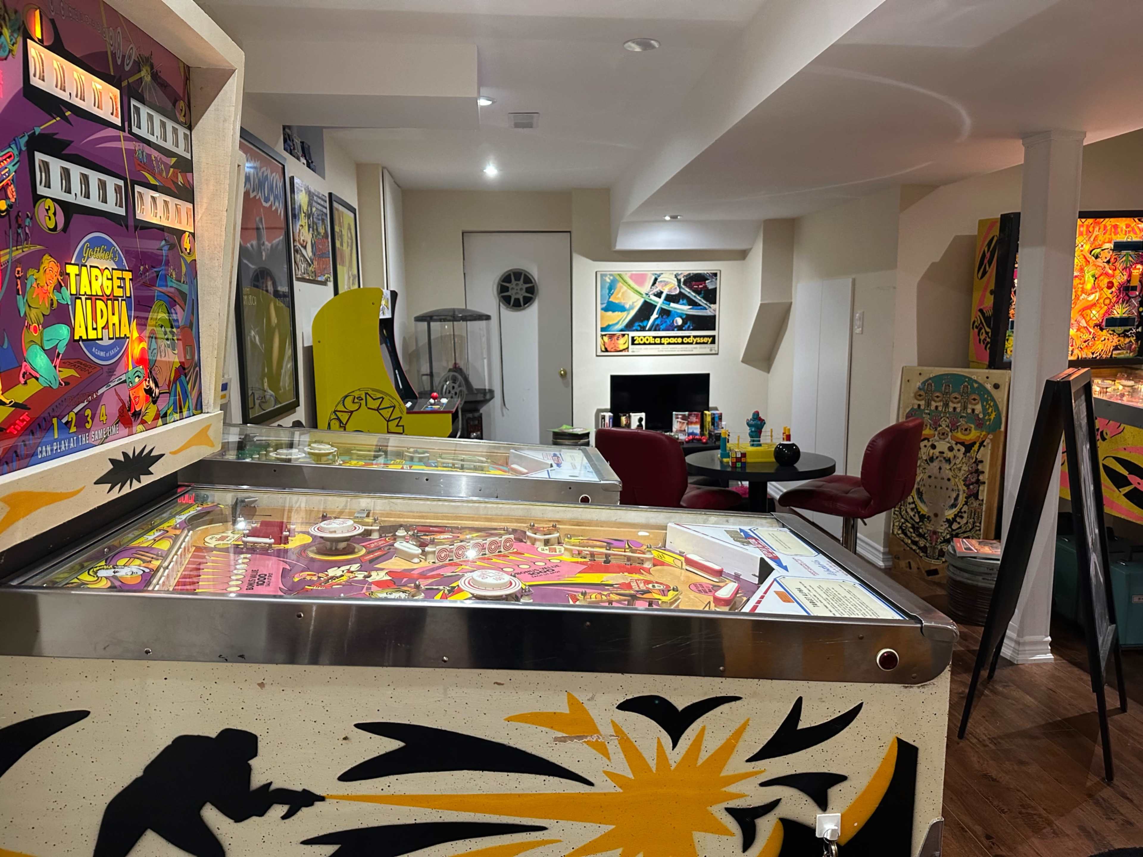The image shows a retro arcade room filled with various pinball machines and colorful game memorabilia.