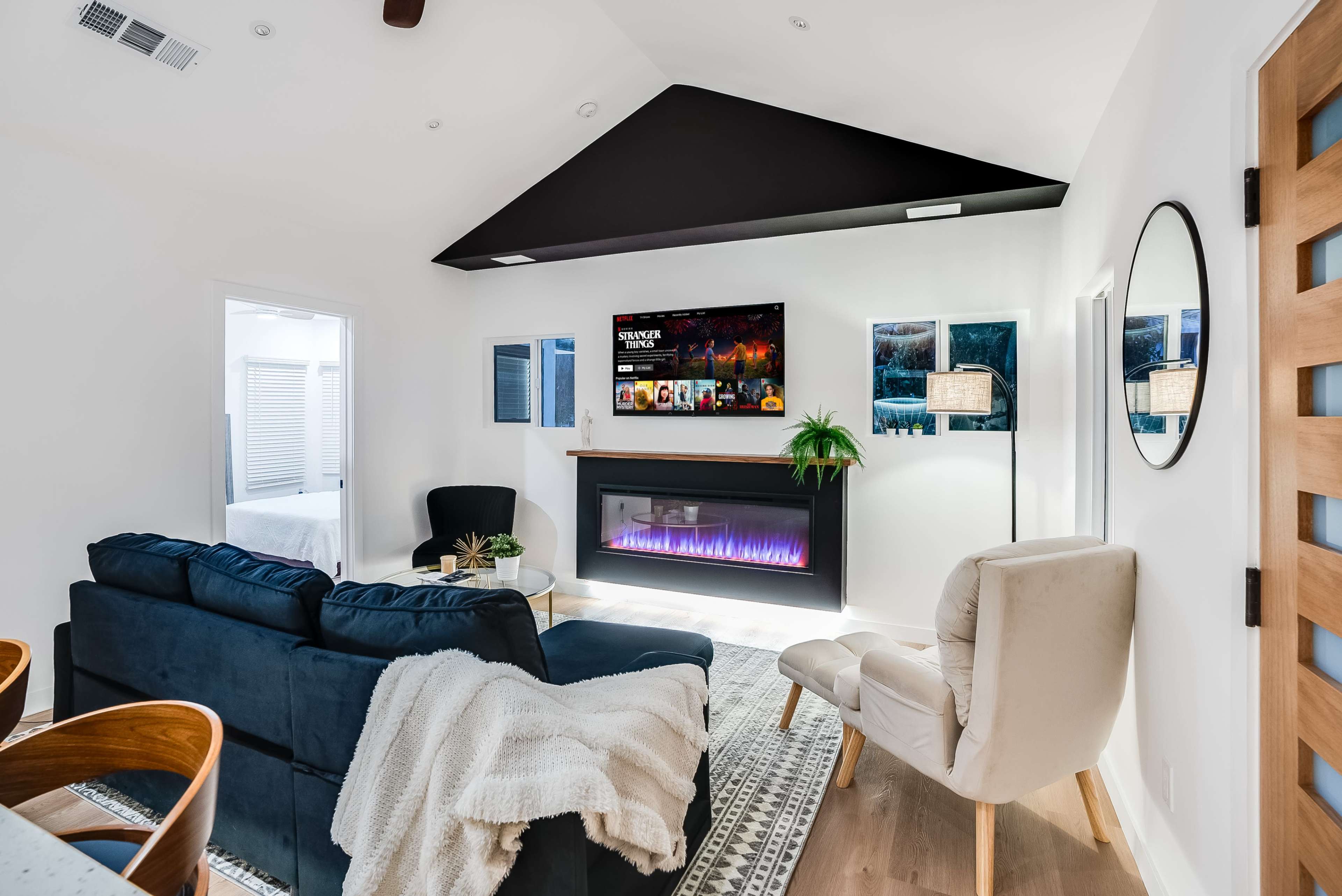 The living room features a blue sofa, a white armchair, an electric fireplace with an illuminated display, and a wall-mounted television.