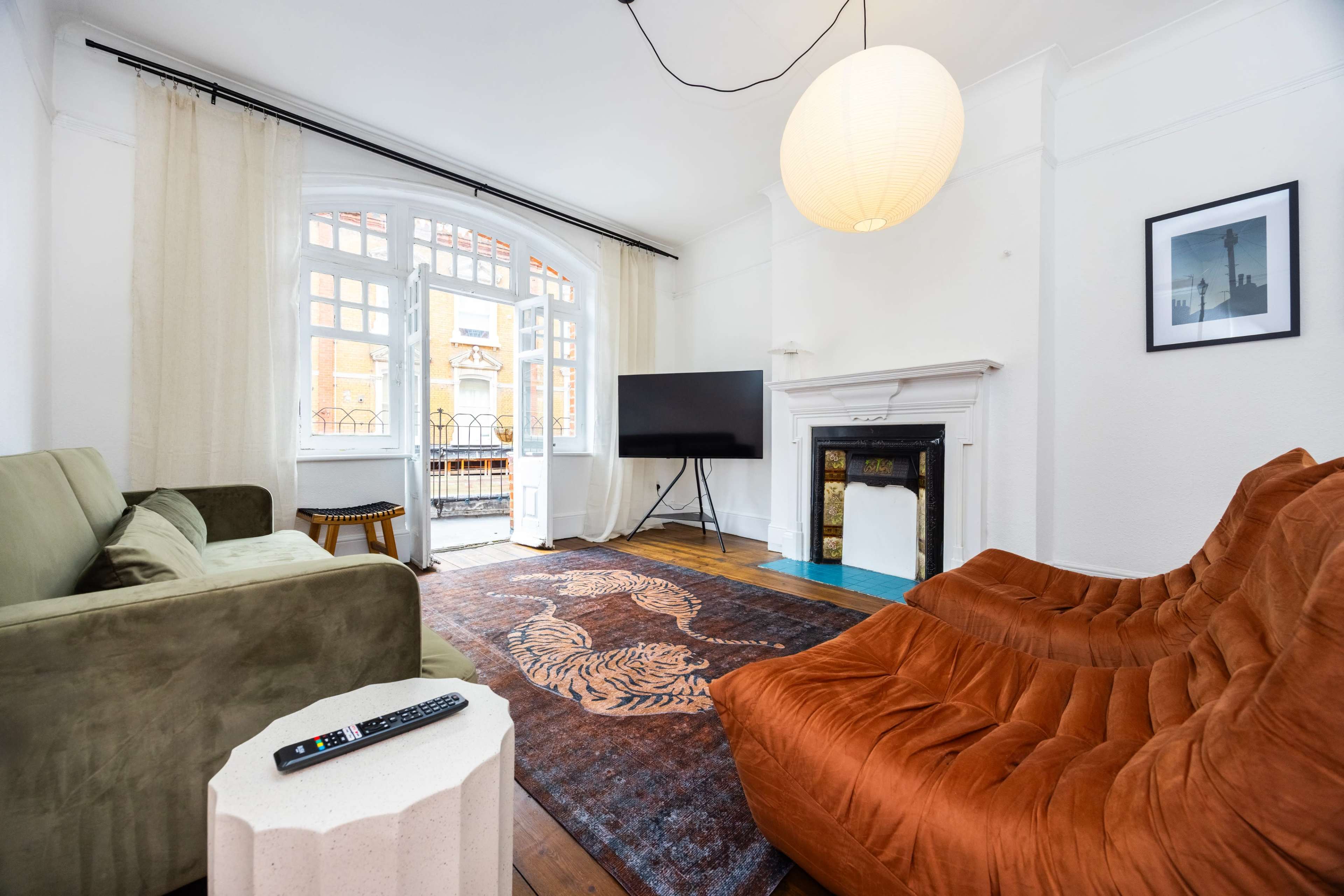 The image shows a living room with two distinct seating areas, a television, and large windows allowing natural light to enter.