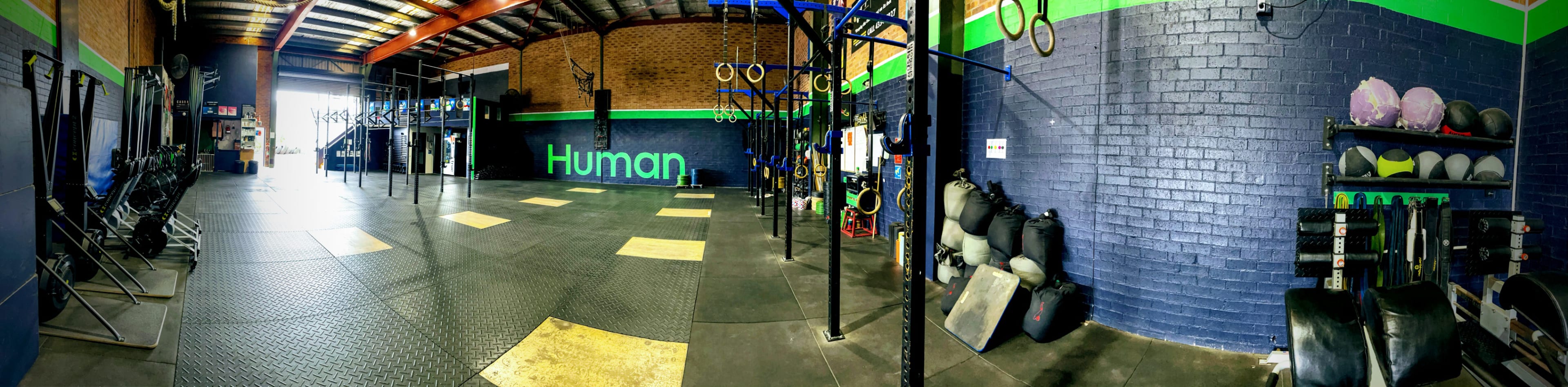 A spacious gym interior with exercise equipment, including pull-up bars and weights, and a large "Human" mural on the wall.