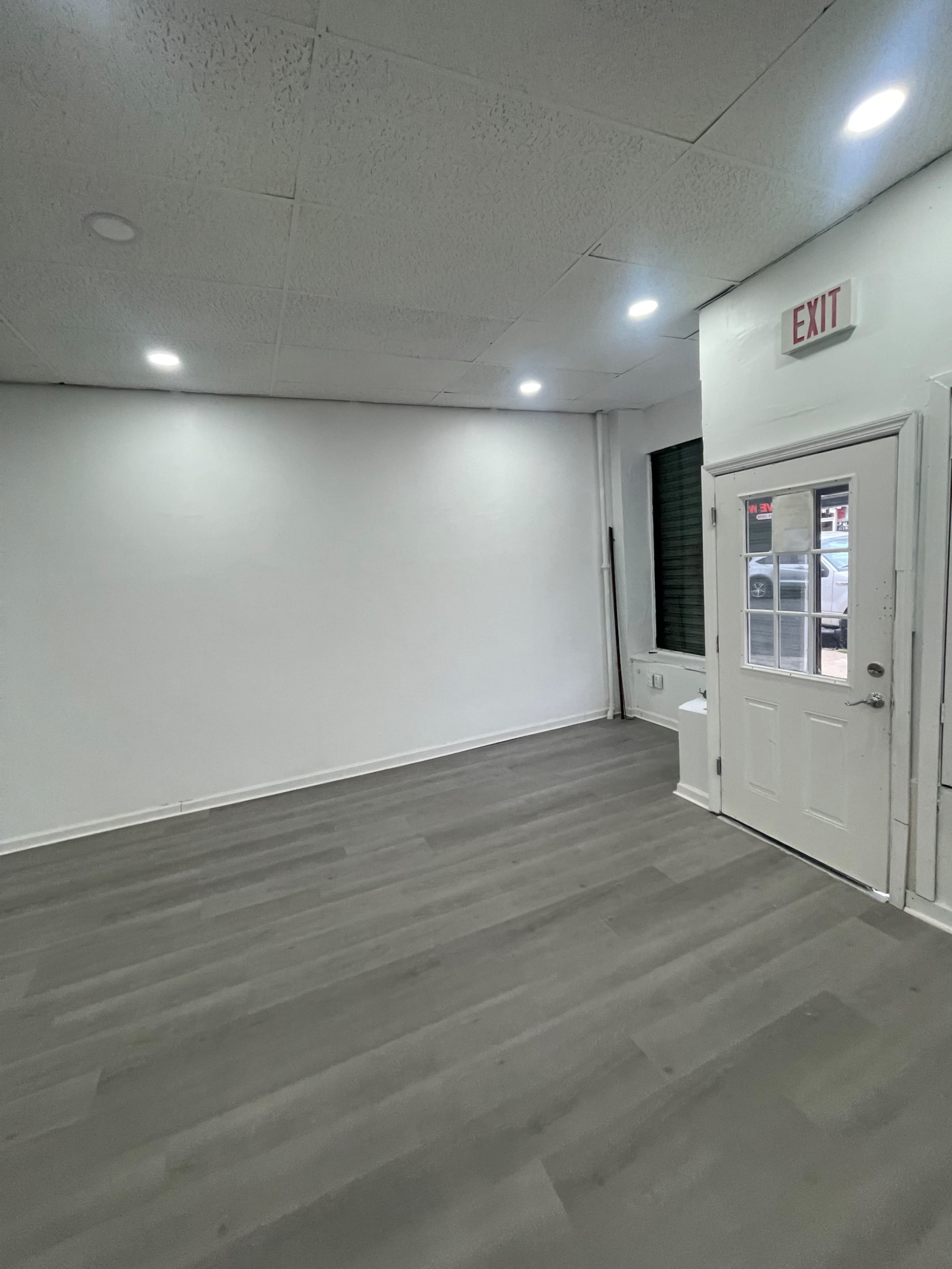 A vacant room with gray flooring, white walls, and an exit door on one side.
