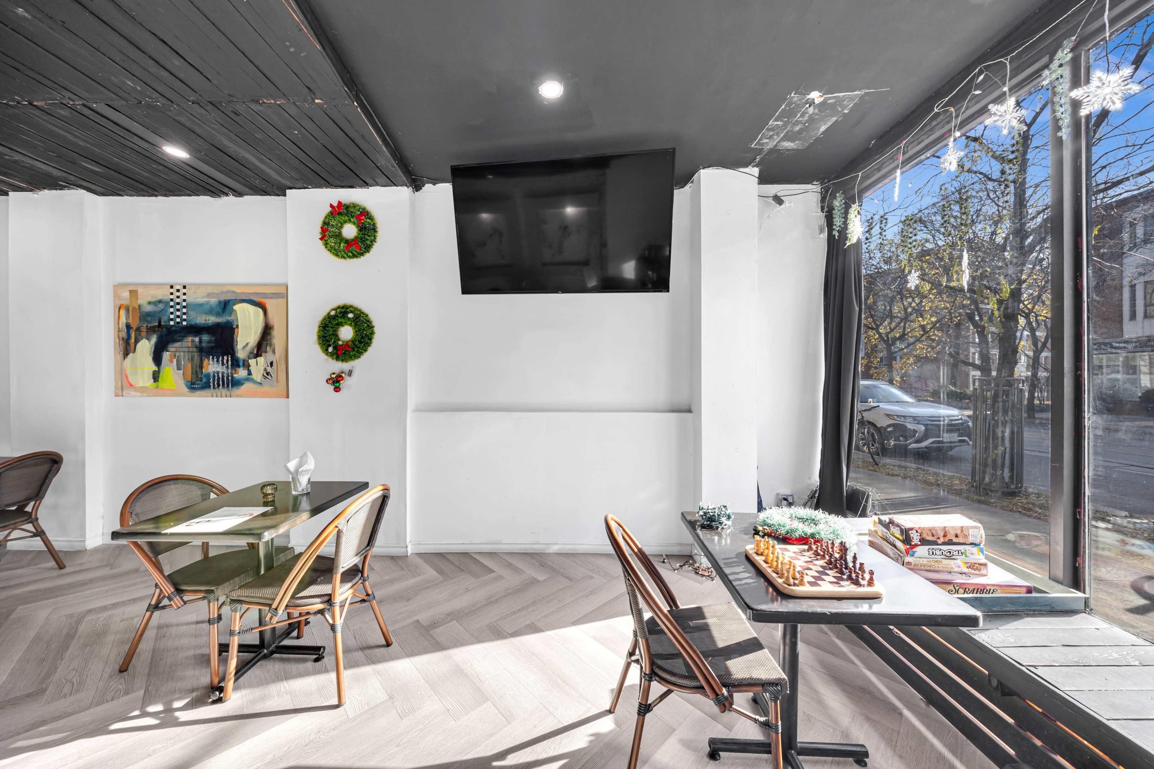 The image shows a cozy cafe interior with wooden chairs and tables, a large wall-mounted TV, and holiday decorations on the walls, including wreaths.