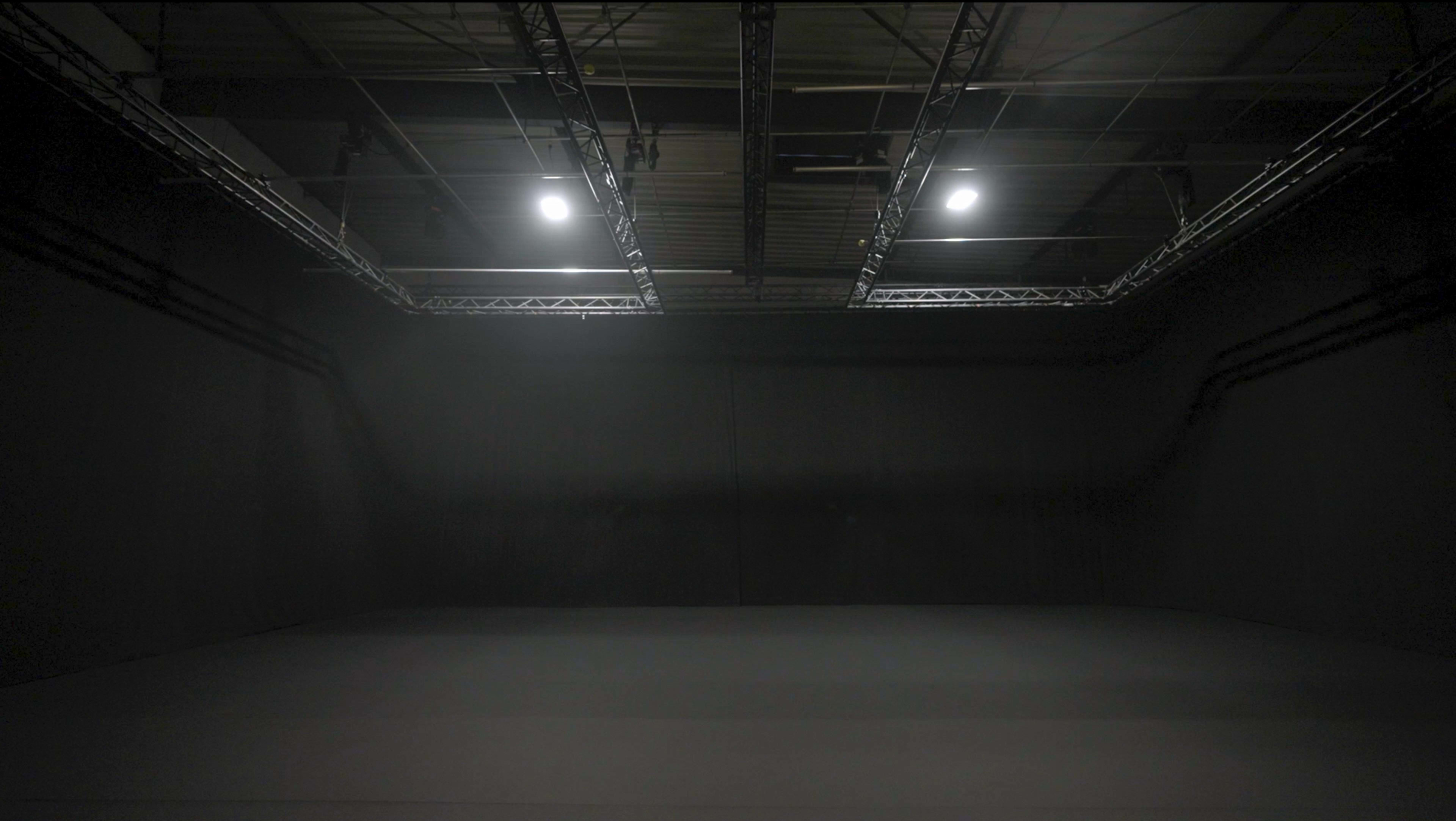 The image shows a large, dimly lit studio space with black walls and overhead lighting.