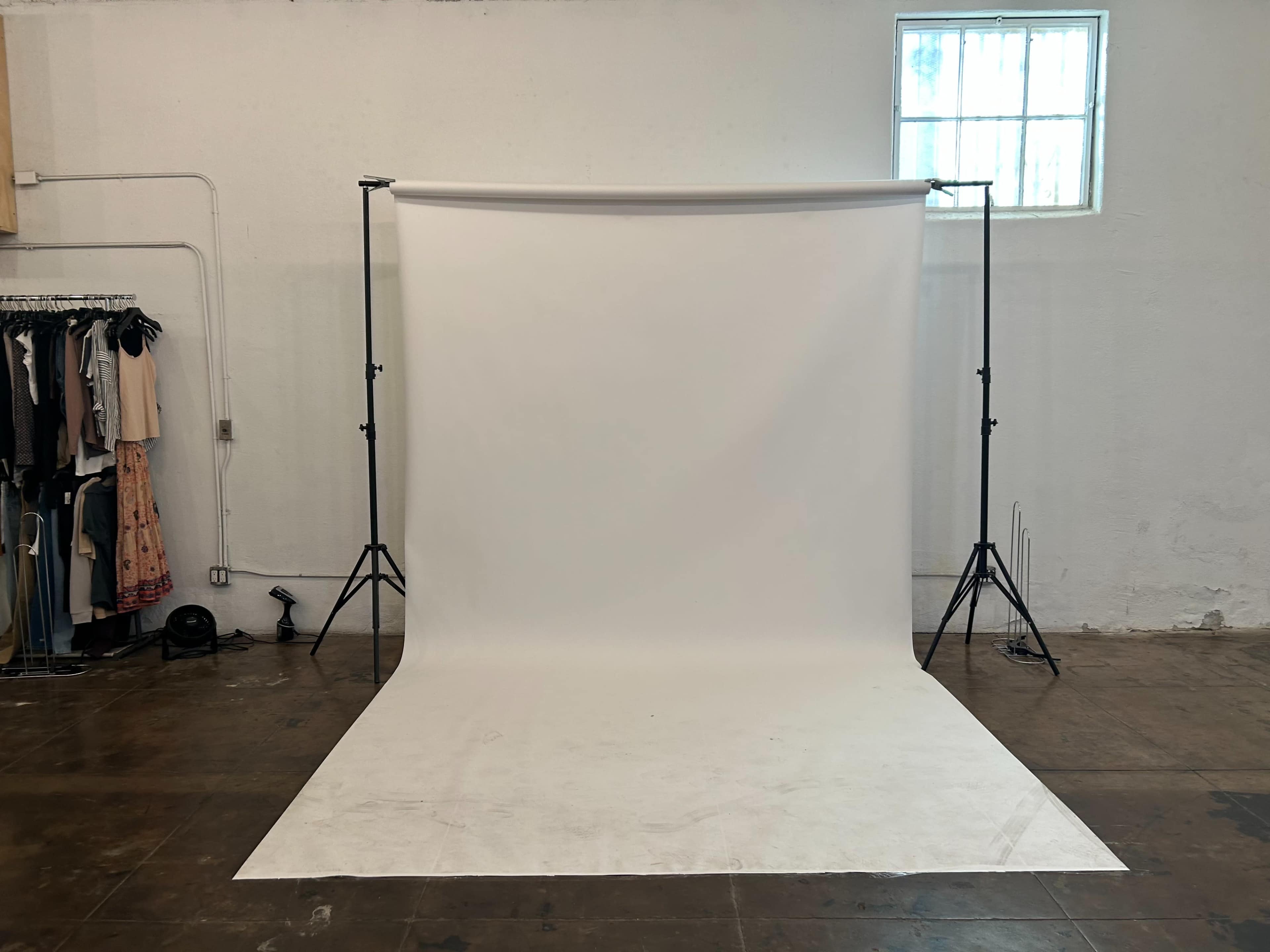 An empty photography studio with a white backdrop supported by two black stands.