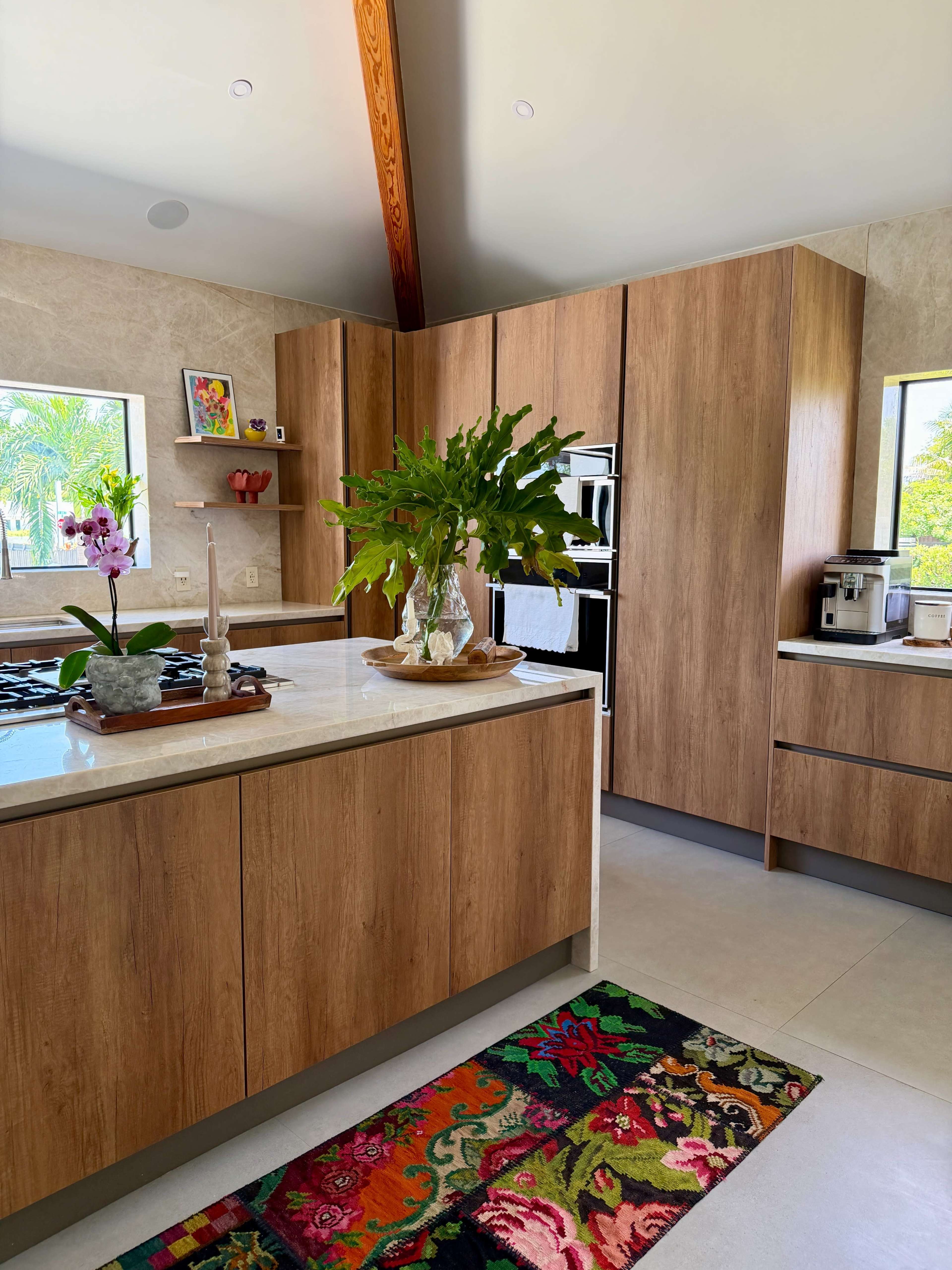 The kitchen features wooden cabinetry, a large island with a marble countertop, and a colorful rug on the floor.