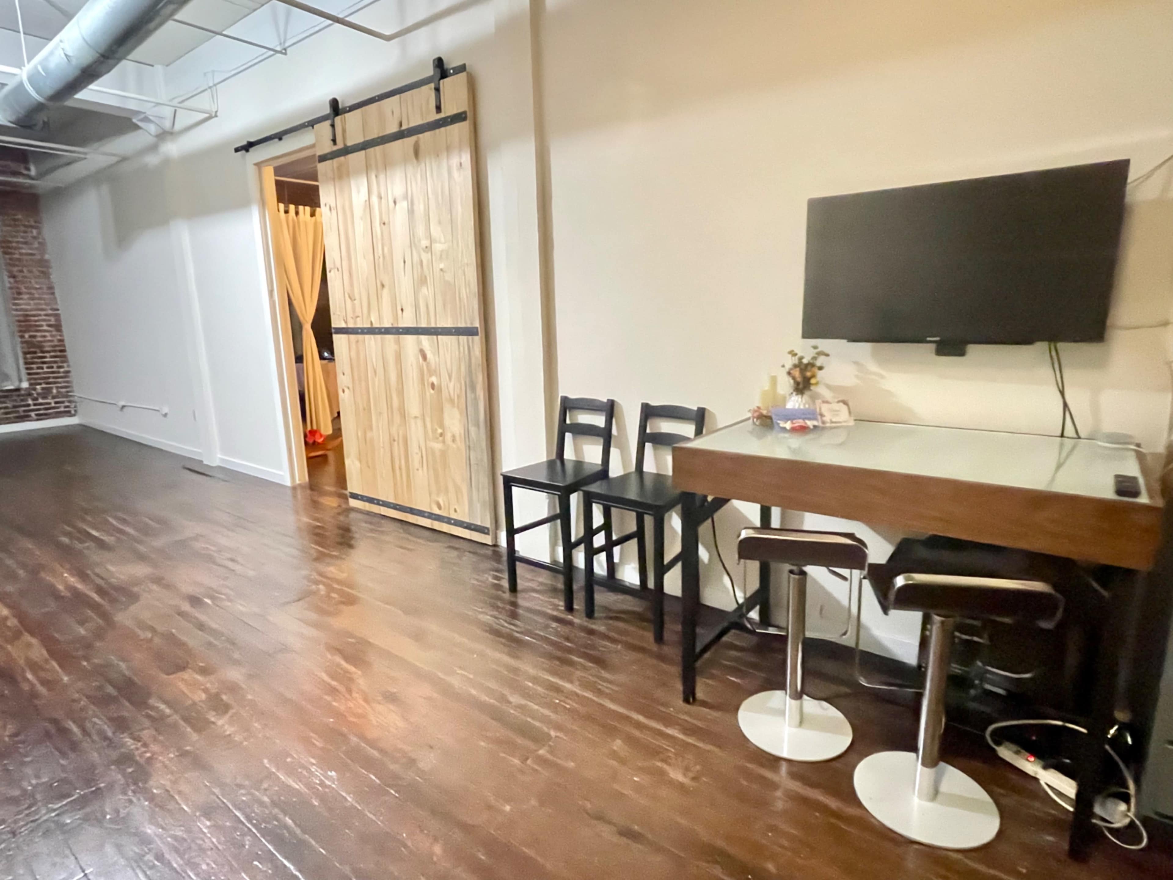 A spacious room with a wooden floor featuring a small dining table and chairs on one side, and a sliding door leading to another area on the opposite side.