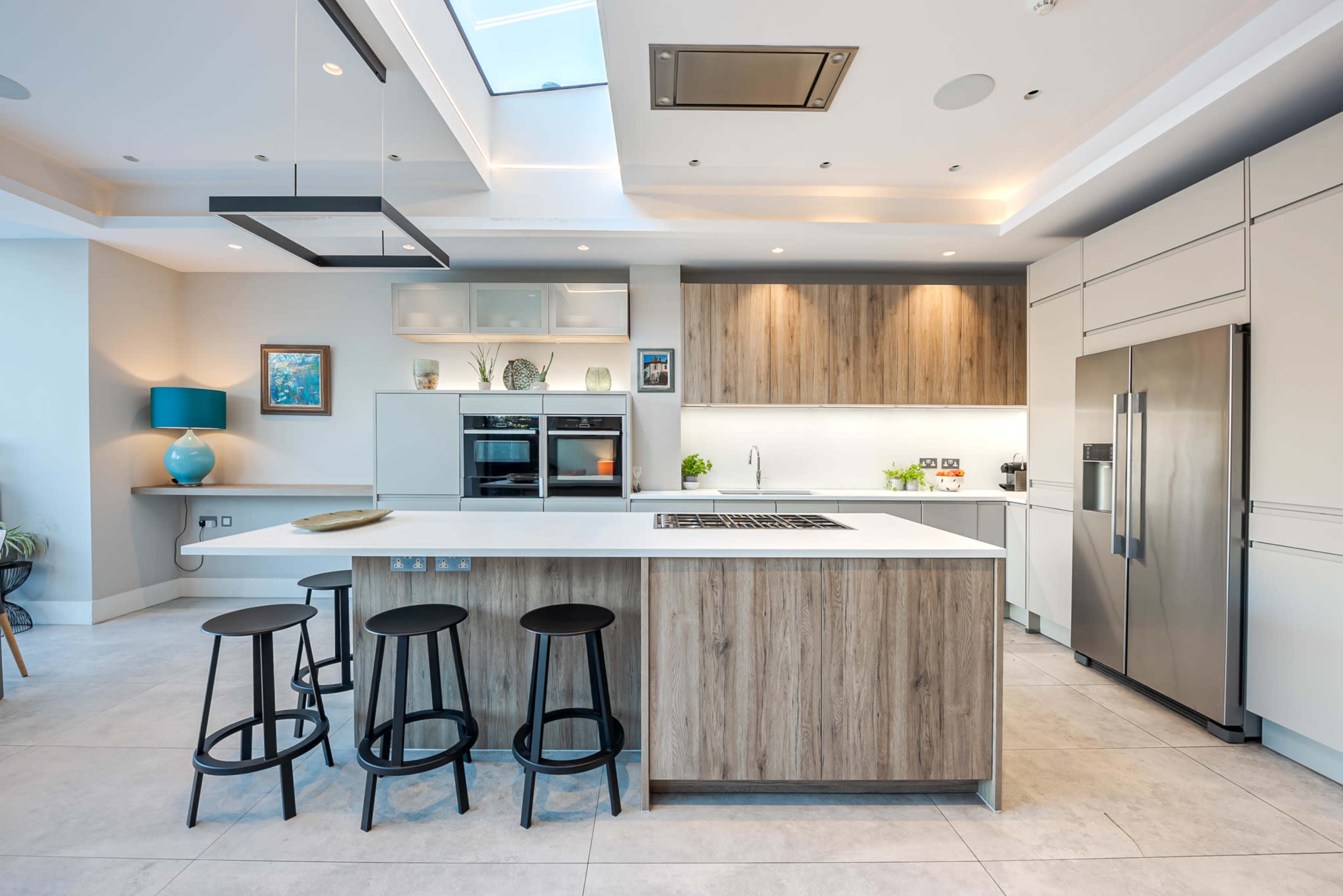 A modern kitchen featuring a large island with bar stools, sleek cabinetry, and stainless steel appliances, illuminated by natural light from a sky light.