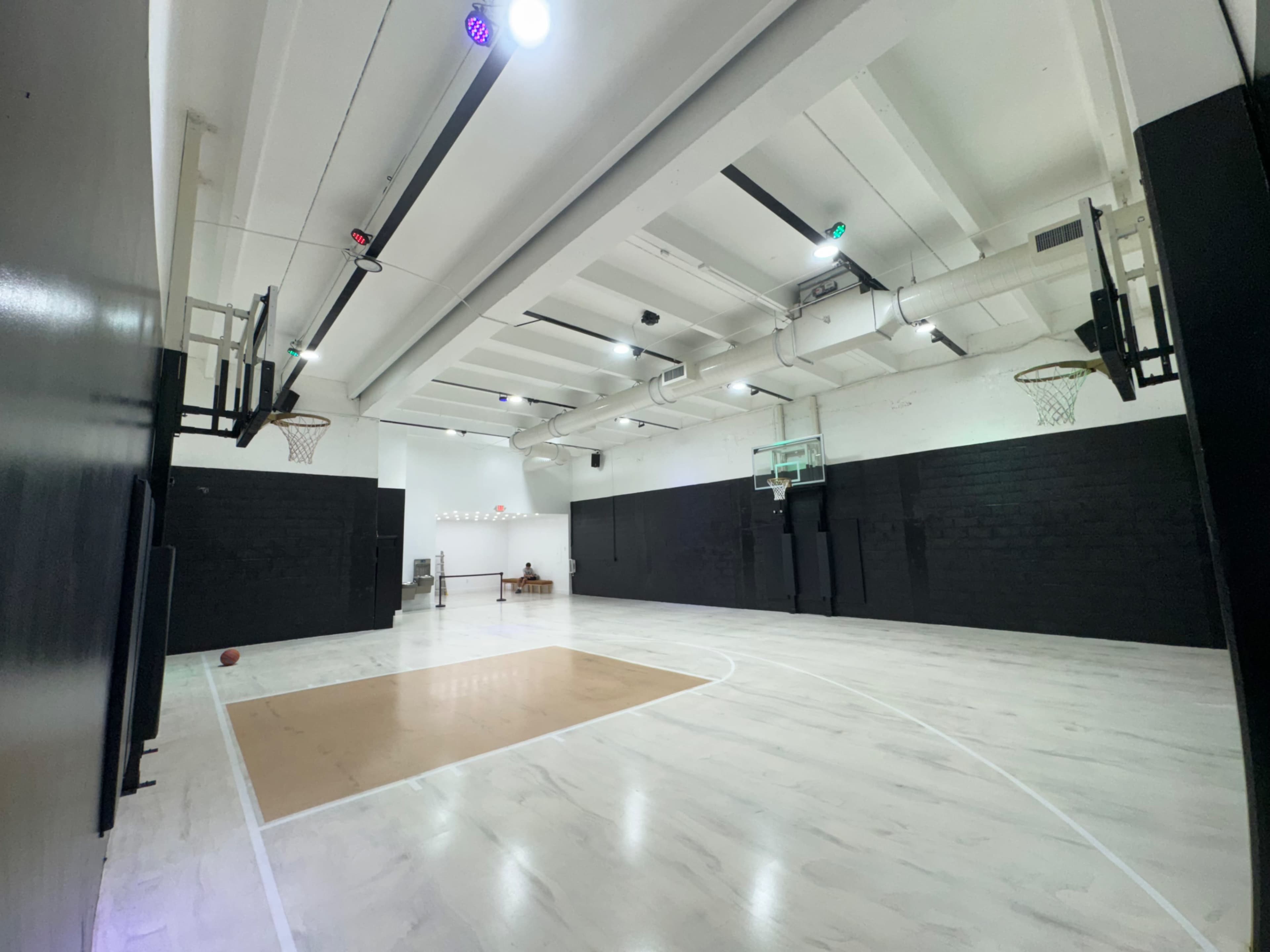 The image shows an indoor basketball court with two basketball hoops and a smooth, light-colored floor.