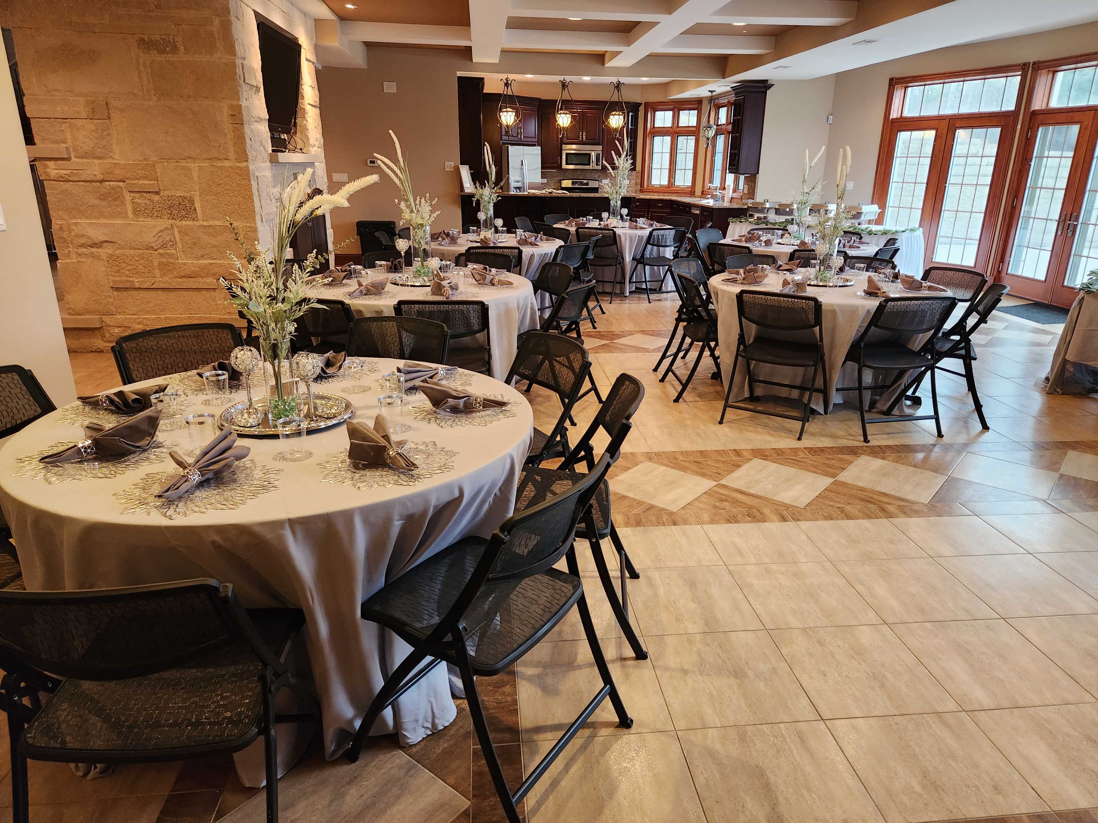 A neatly arranged dining area with several round tables covered in tablecloths, each set with dishes and centerpieces, surrounded by black folding chairs.