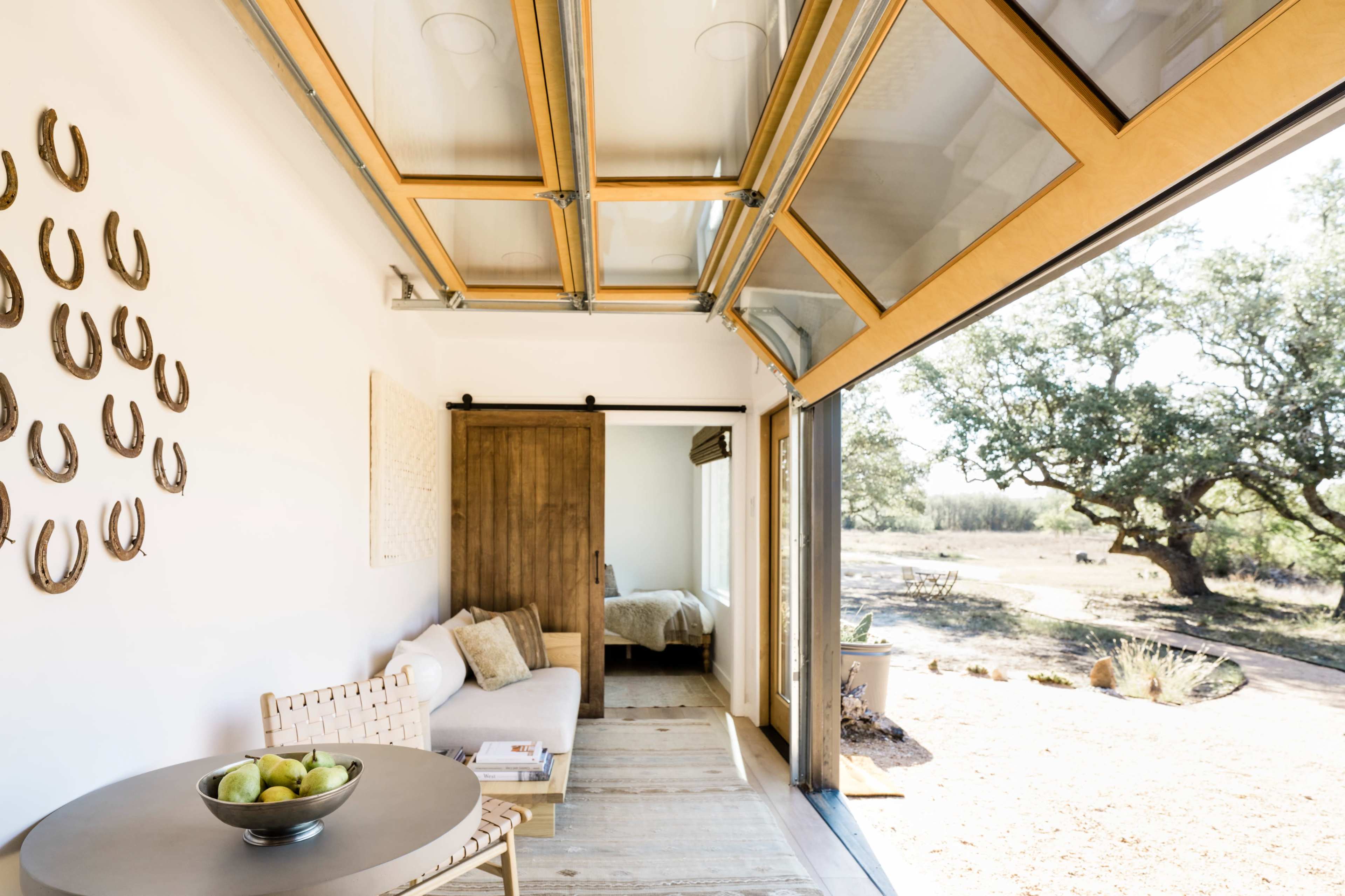 A modern, open-concept interior features sliding glass doors that lead to an outdoor space, with a seating area, a round table, and decorative wall art.