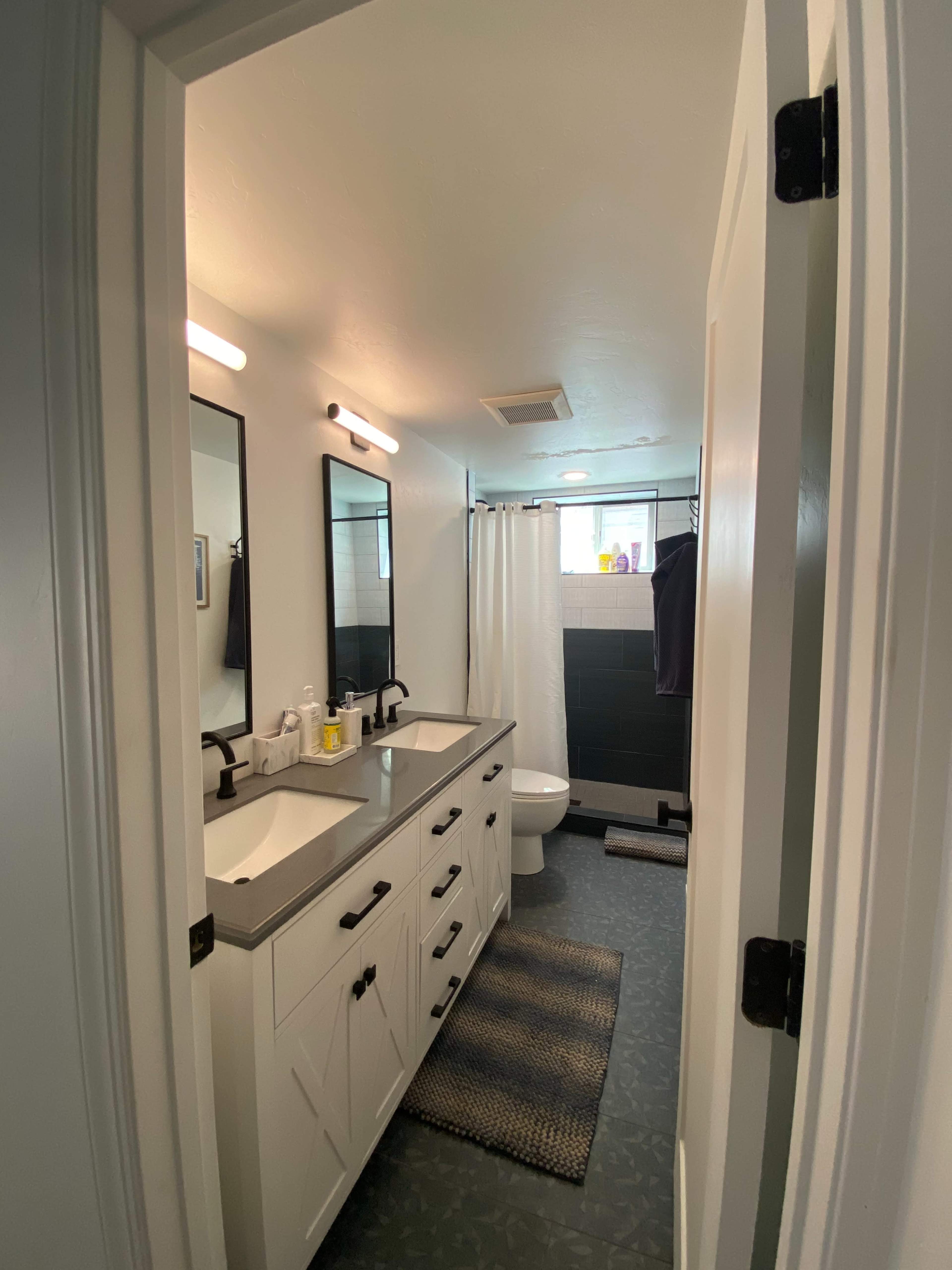 A modern bathroom with two sinks, dark tile walls, a shower curtain, and mirrors above each sink.