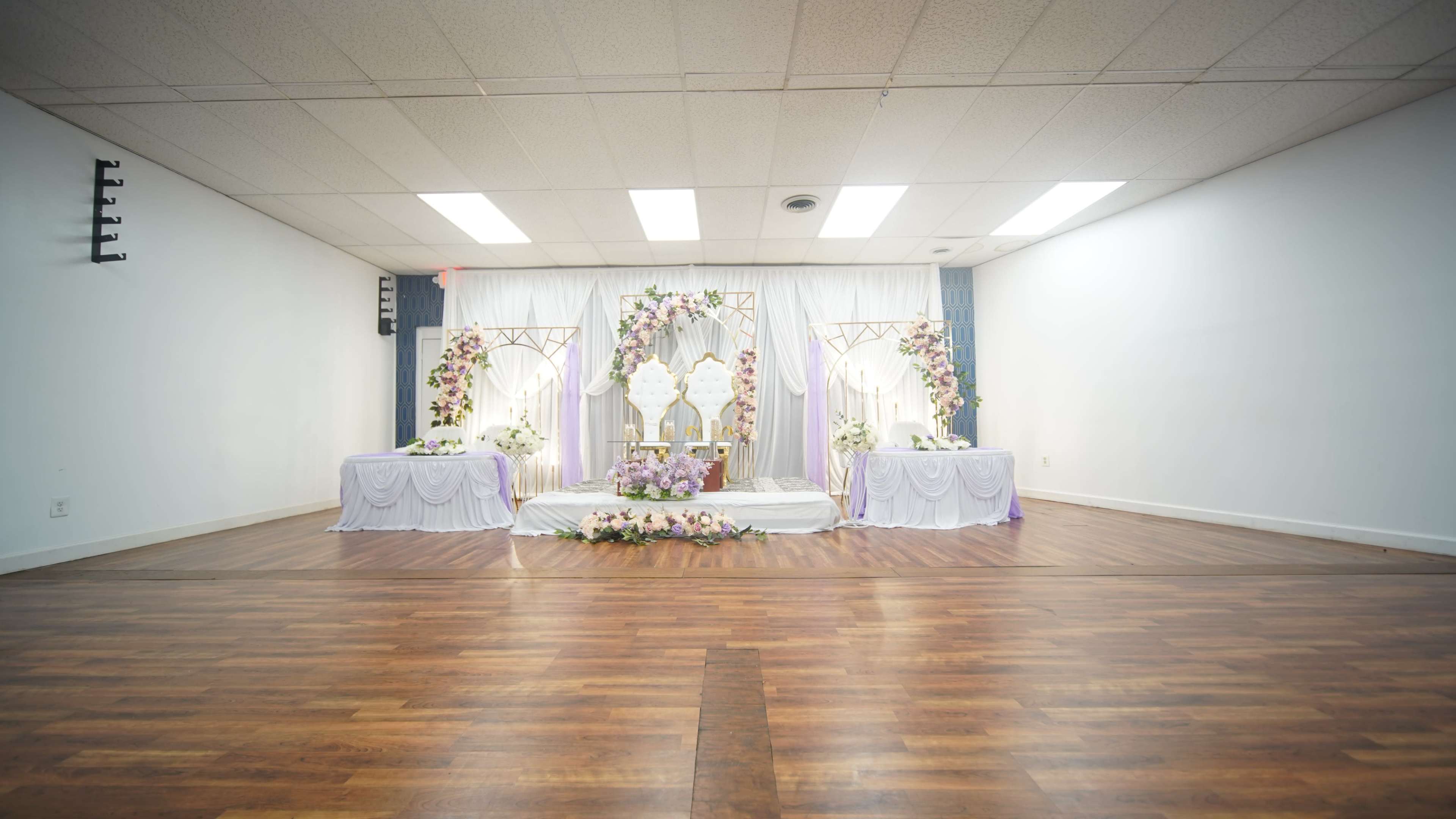 The image shows a decorated event space with a floral arrangement and two tables set up on a wooden floor.