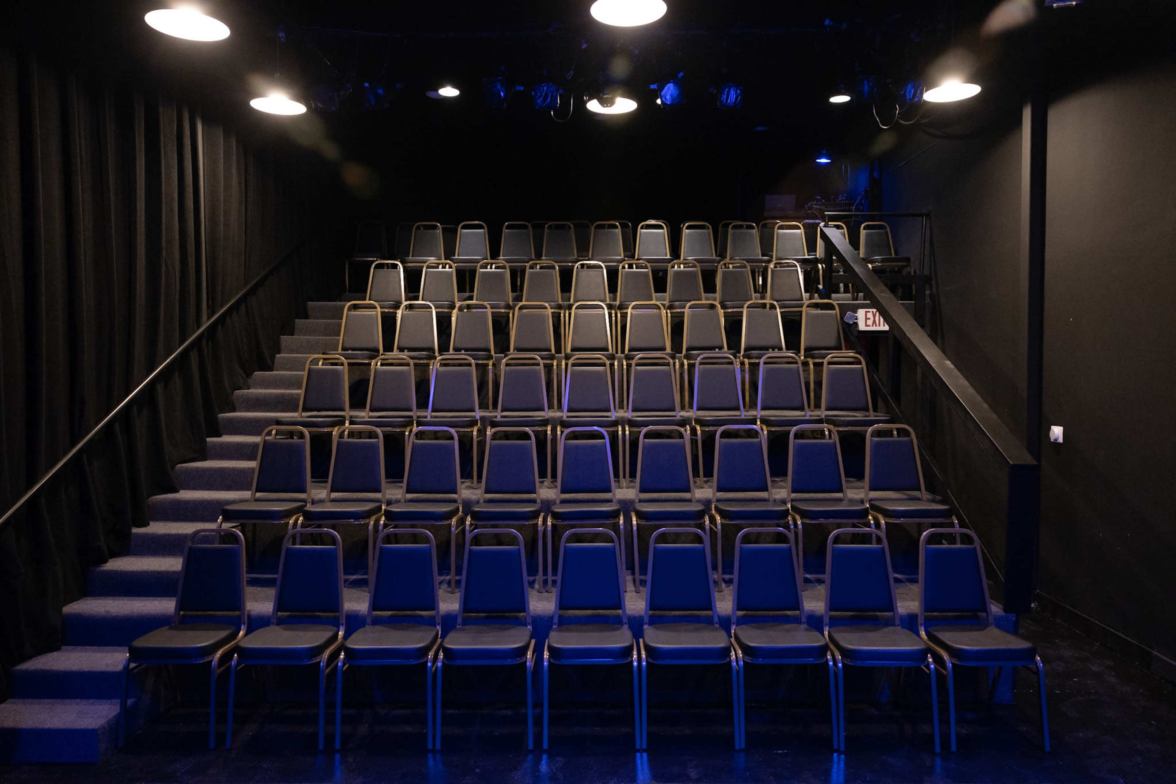 A set of empty, stacked chairs arranged in an ascending seating layout in a dark theater.