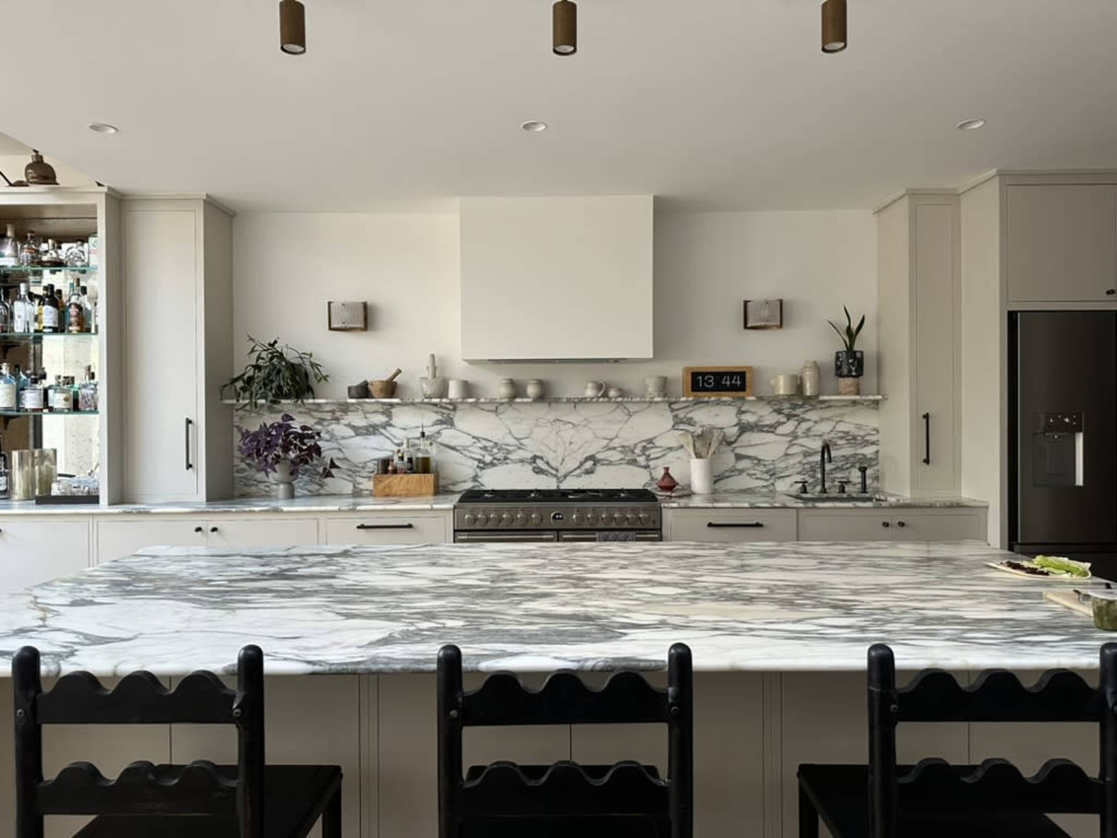 The kitchen features a large marble countertop with a central island, surrounded by black chairs, and includes modern cabinetry and shelving.