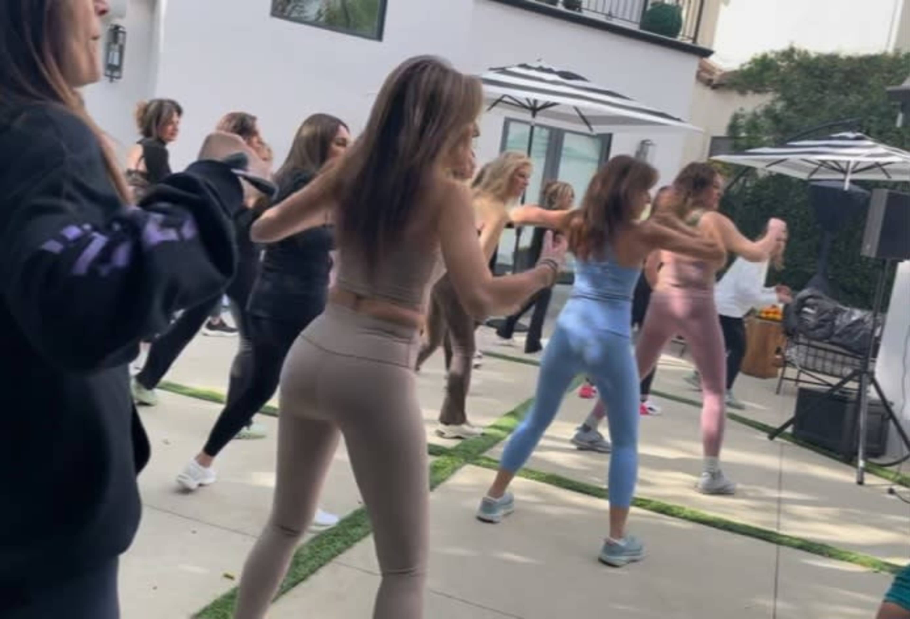 A group of women in athletic wear participate in a fitness class outdoors.