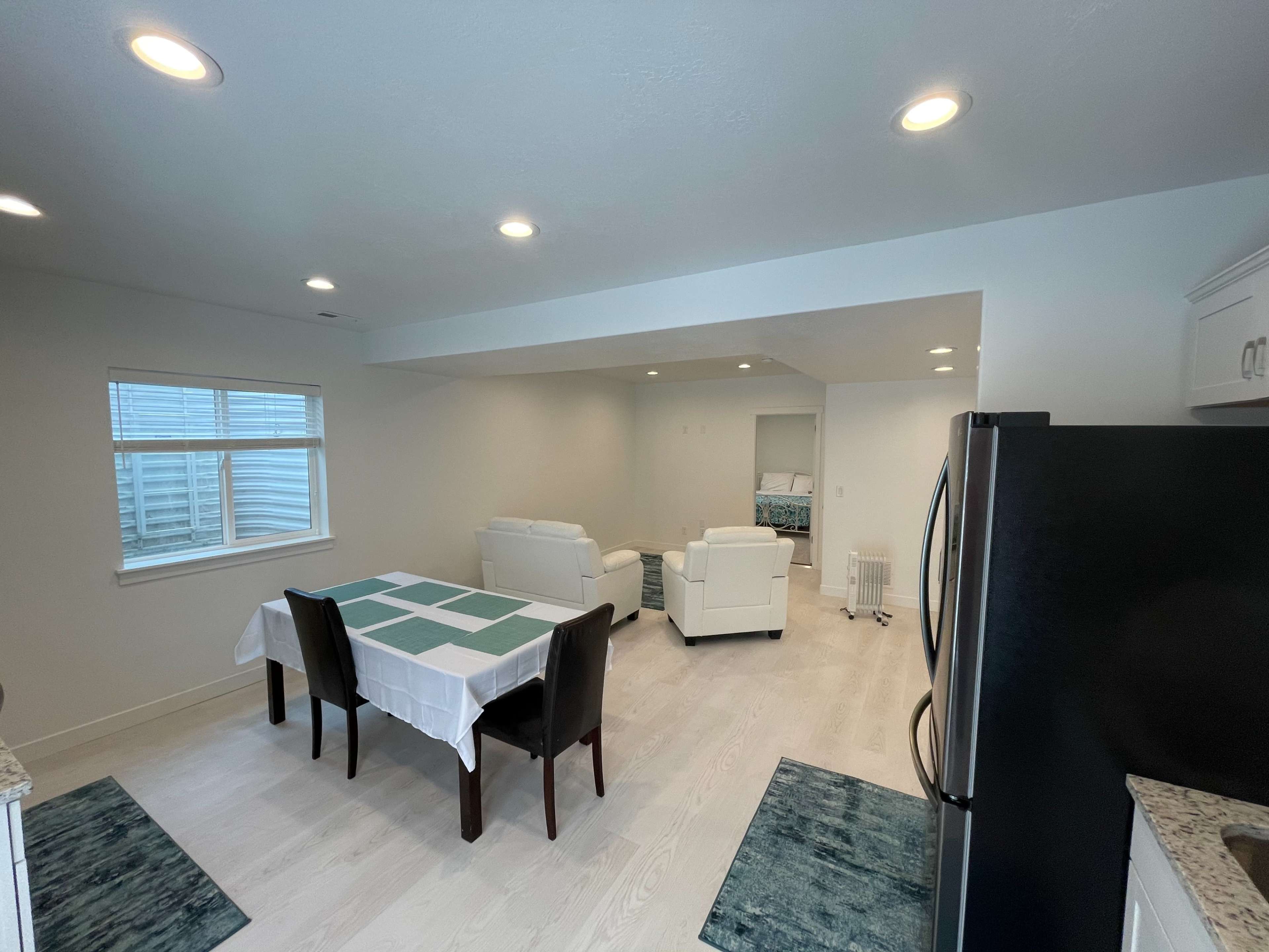 A modern kitchen and dining area features a table with a light blue and white tablecloth, surrounded by four chairs, and two white sofas positioned against a wall.