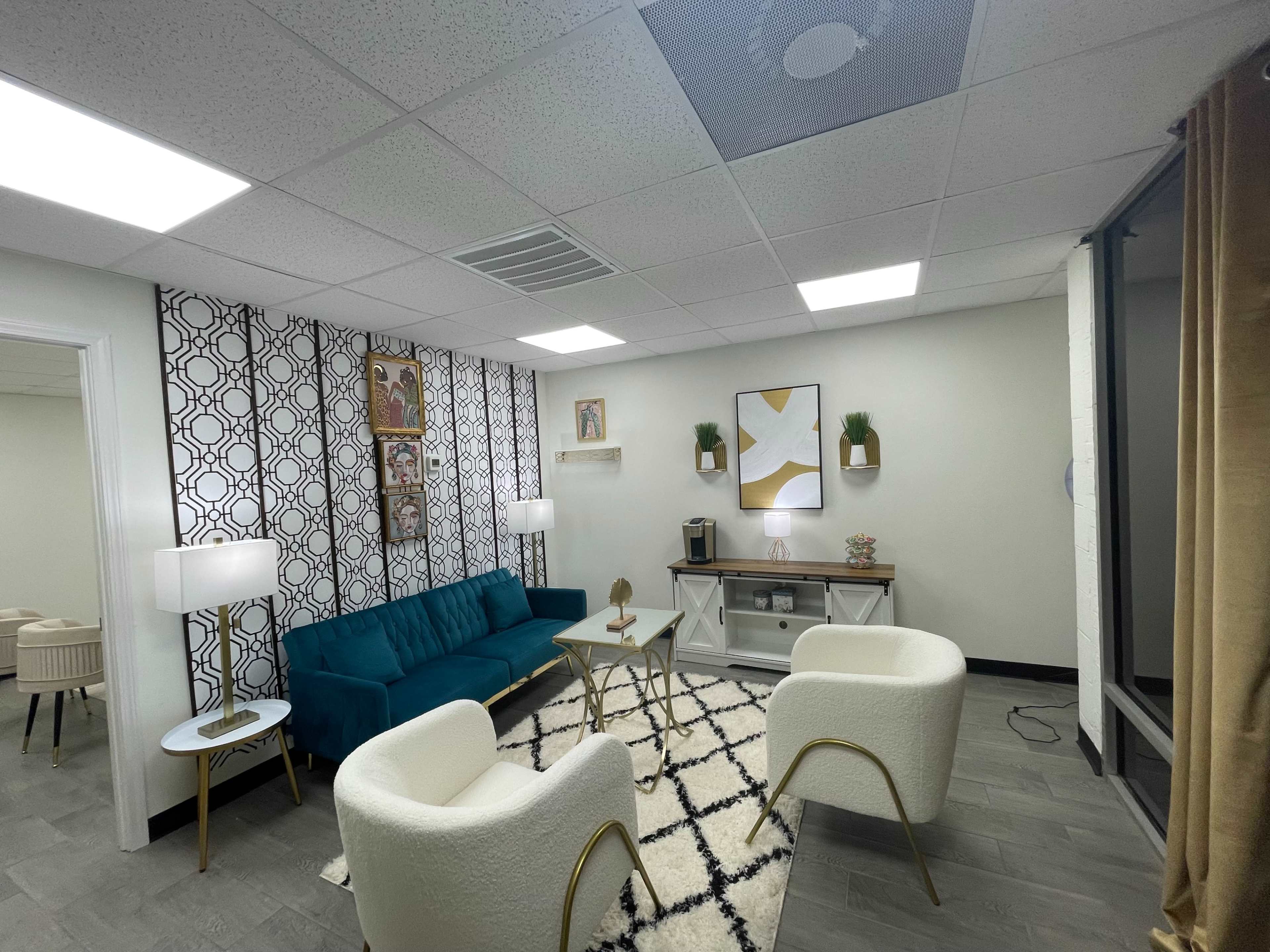 The image shows a modern waiting room with a teal sofa, two white armchairs, a coffee table, and decorative wall art.