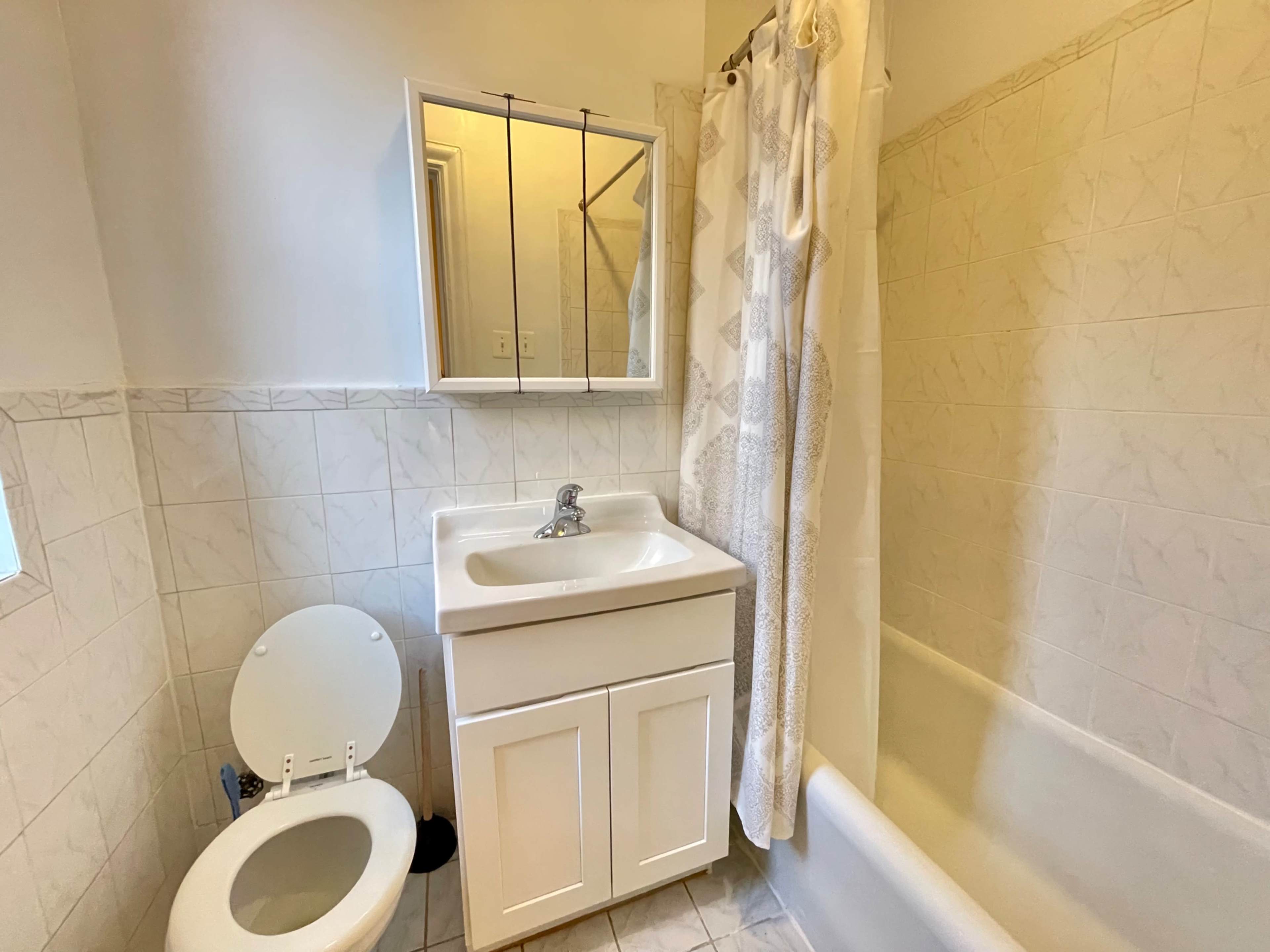 The image shows a small bathroom featuring a bathtub, a toilet, and a sink with a mirror above it.