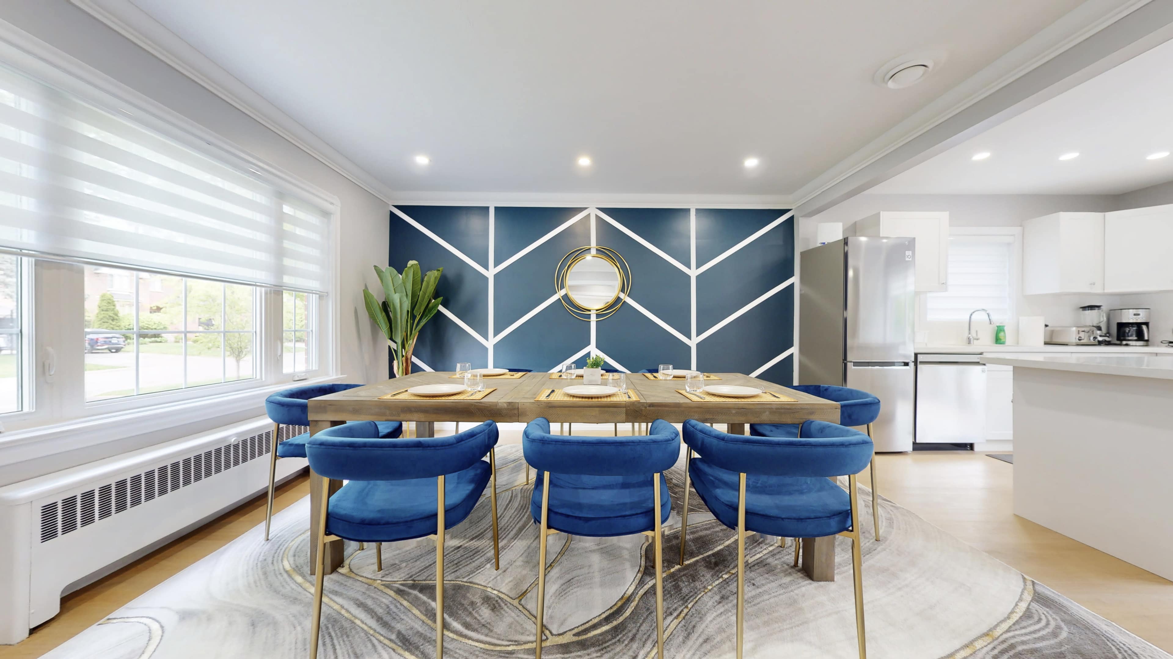 A modern dining area with a large wooden table surrounded by blue chairs, set against a blue geometric accent wall.