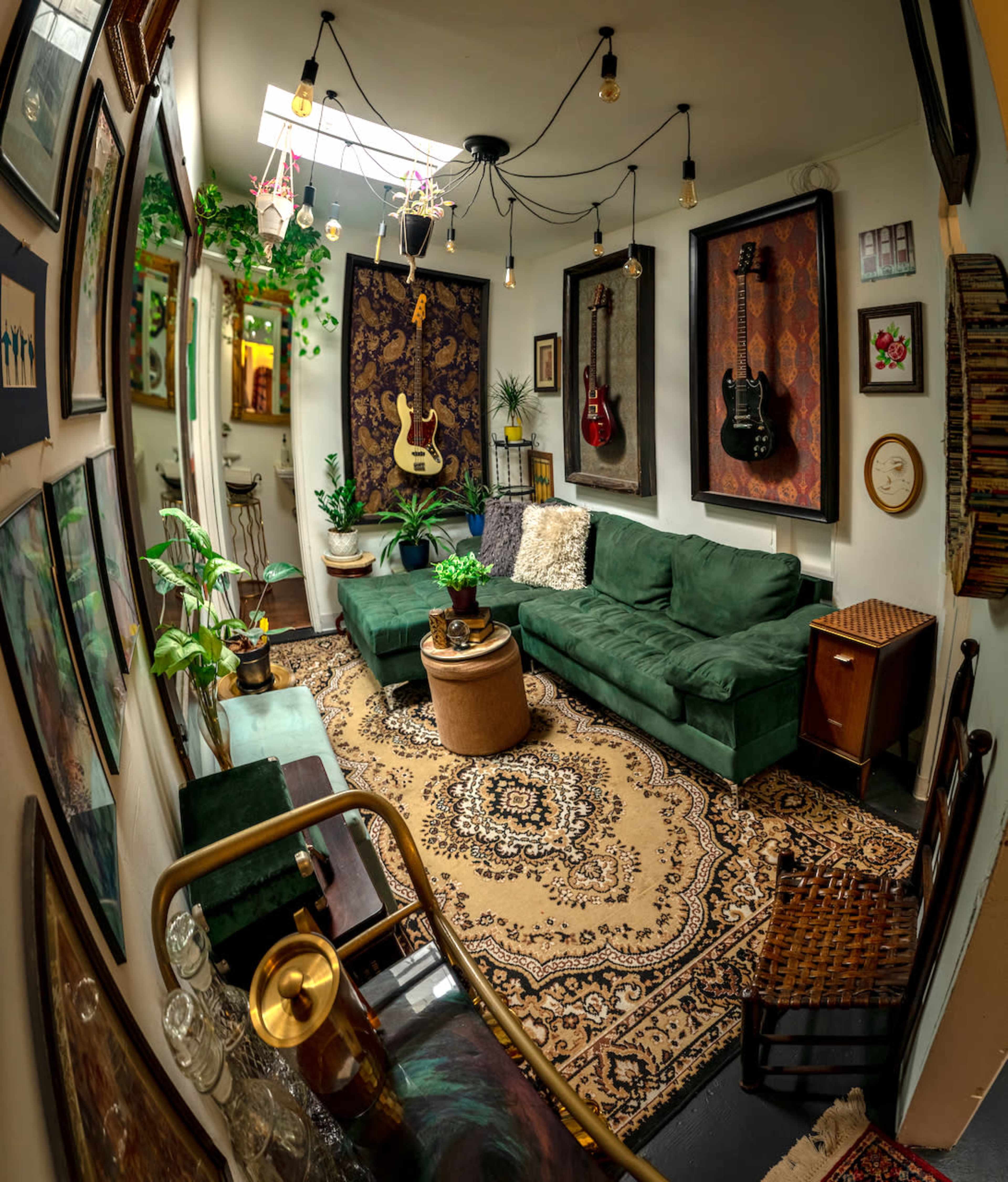 The image shows a cozy living room featuring a green sectional sofa, an area rug, wall-mounted guitars, and various plants.