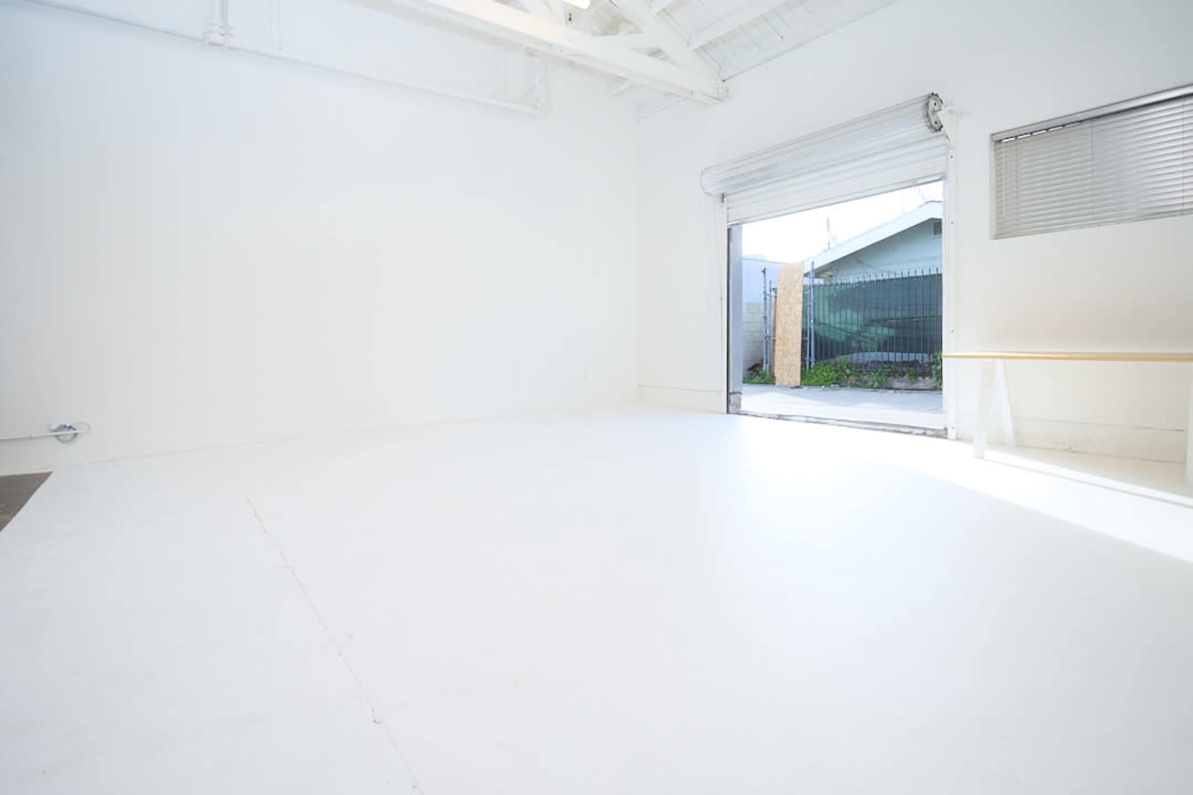 The image shows a bright, empty room with white walls and a large open door leading to an outdoor area.