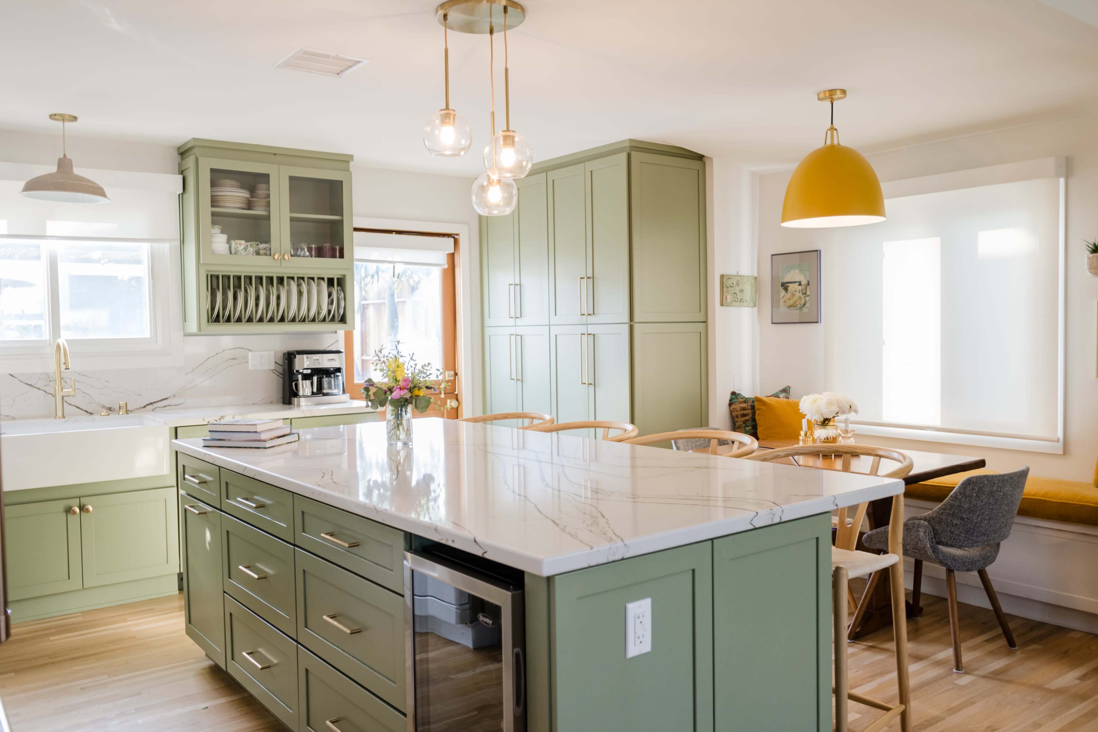 The kitchen features green cabinetry, a marble countertop island, and wooden dining chairs arranged around a table.
