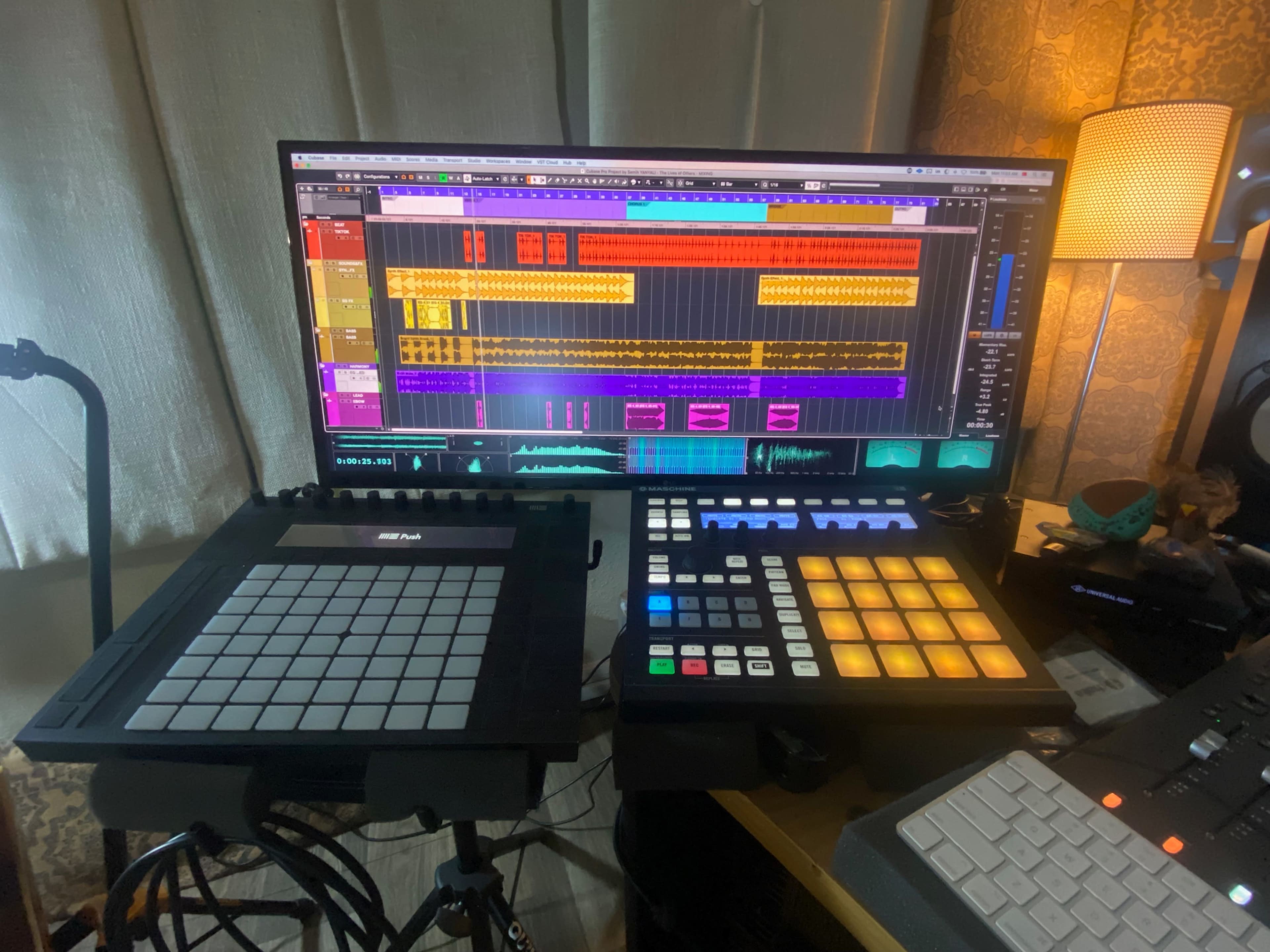 A computer monitor displays a digital audio workstation interface with a colorful music track timeline, while two MIDI controllers are positioned in front of it.