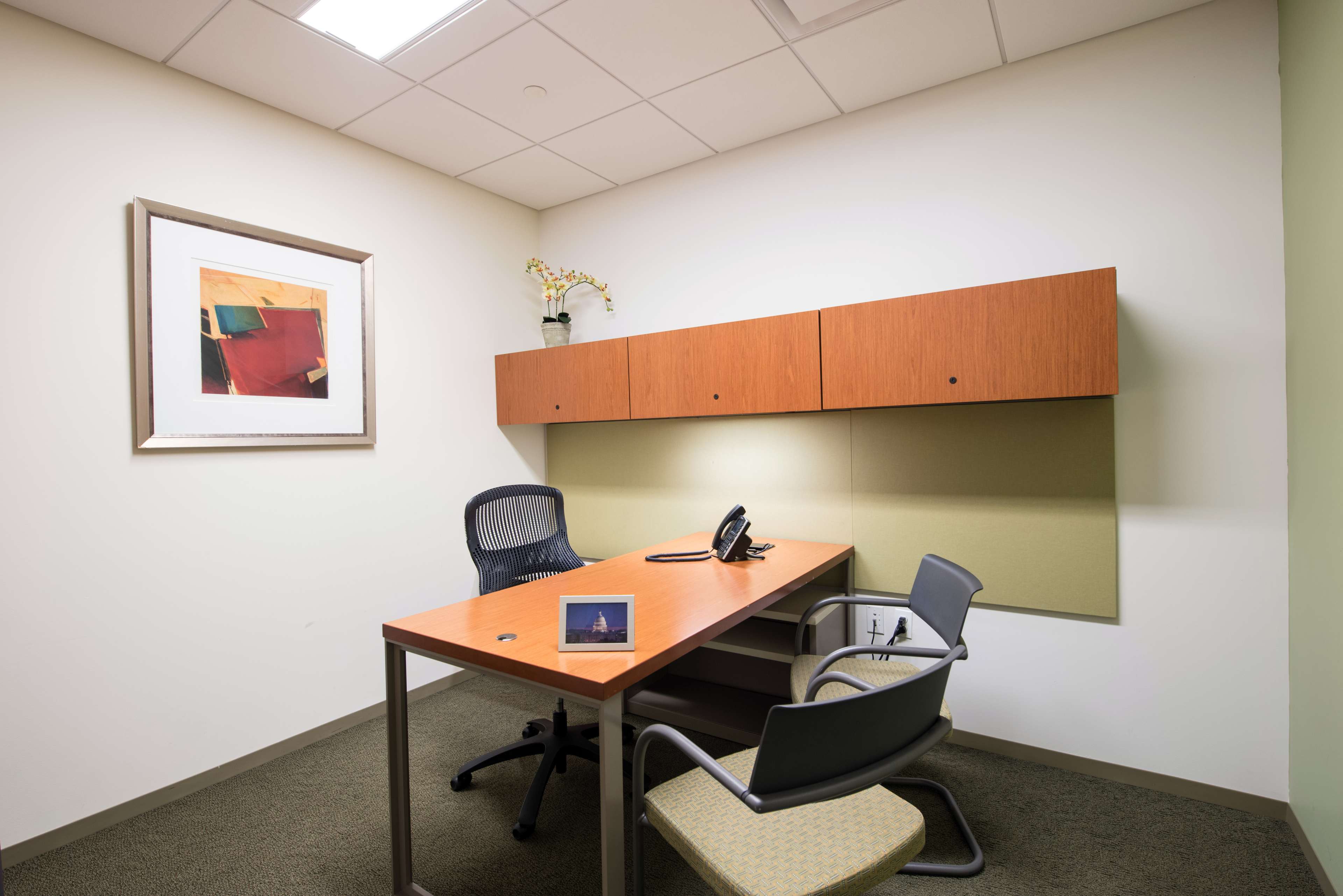 A small office space with a wooden desk, two chairs, a telephone, and wall-mounted storage above the desk.