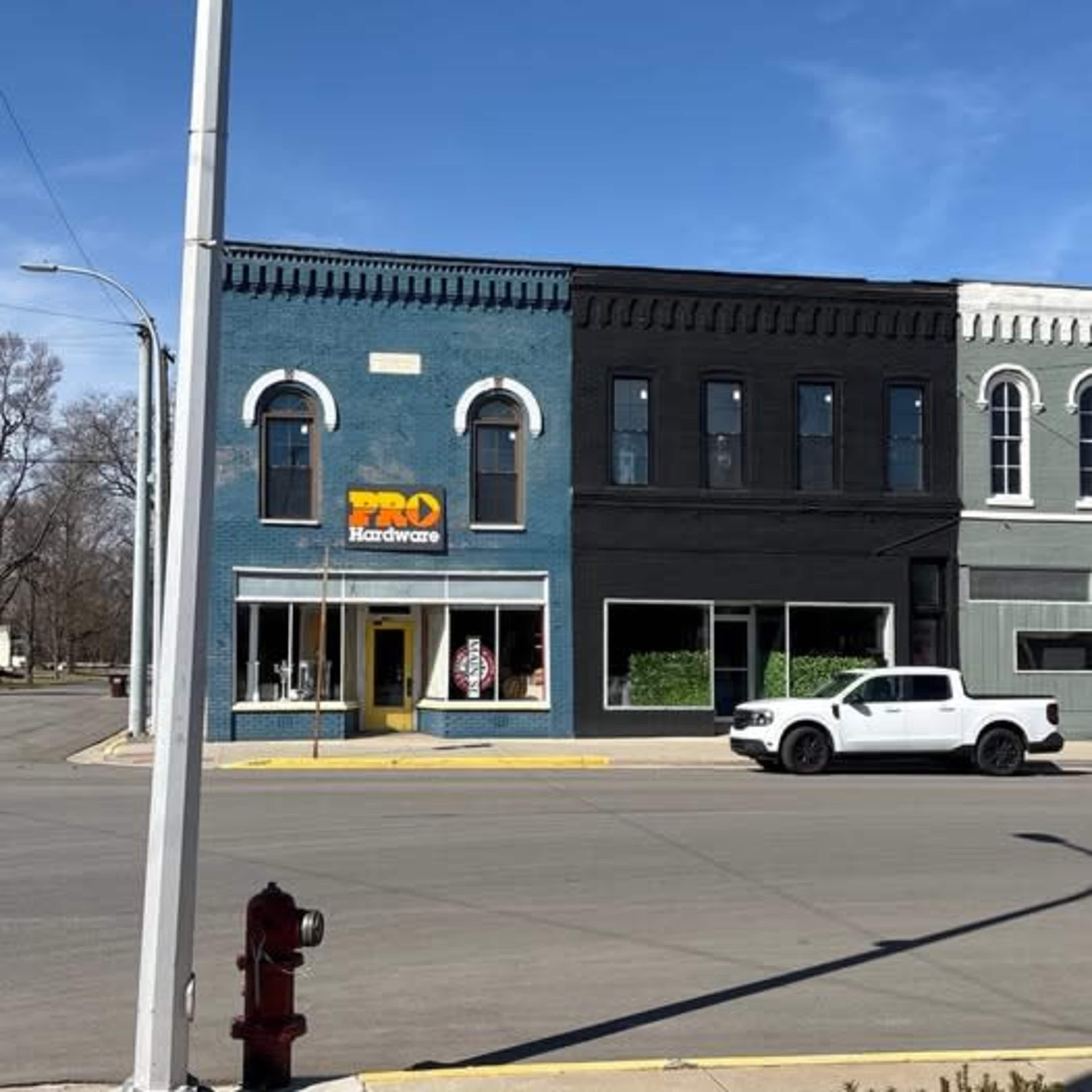 The image shows a street view of a two-story hardware store building with a blue facade and a large sign reading "PRO Hardware," located at a corner intersection.
