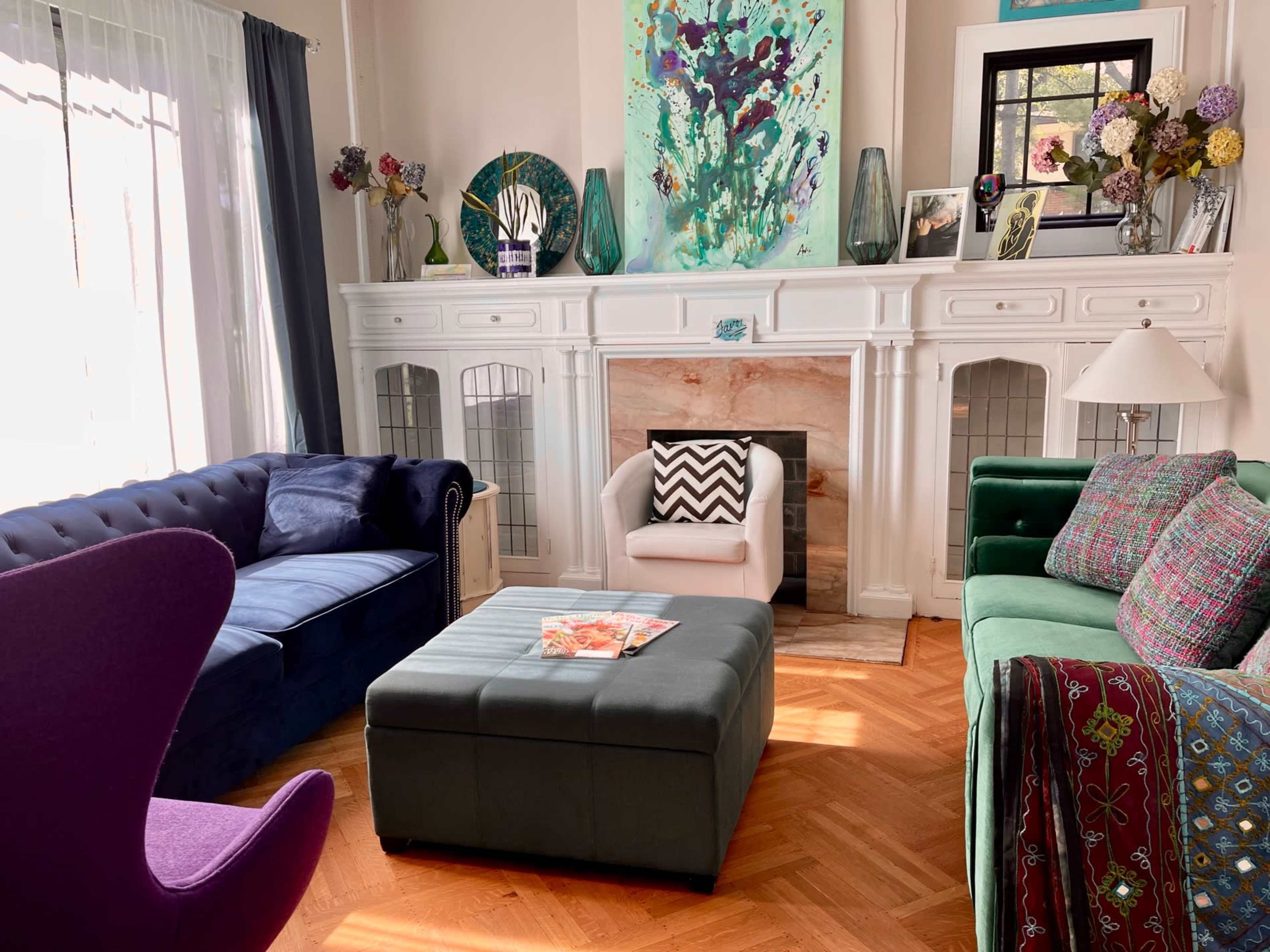 The living room features a mix of colorful couches, a coffee table with a magazine, and a decorative fireplace surrounded by art and vases.