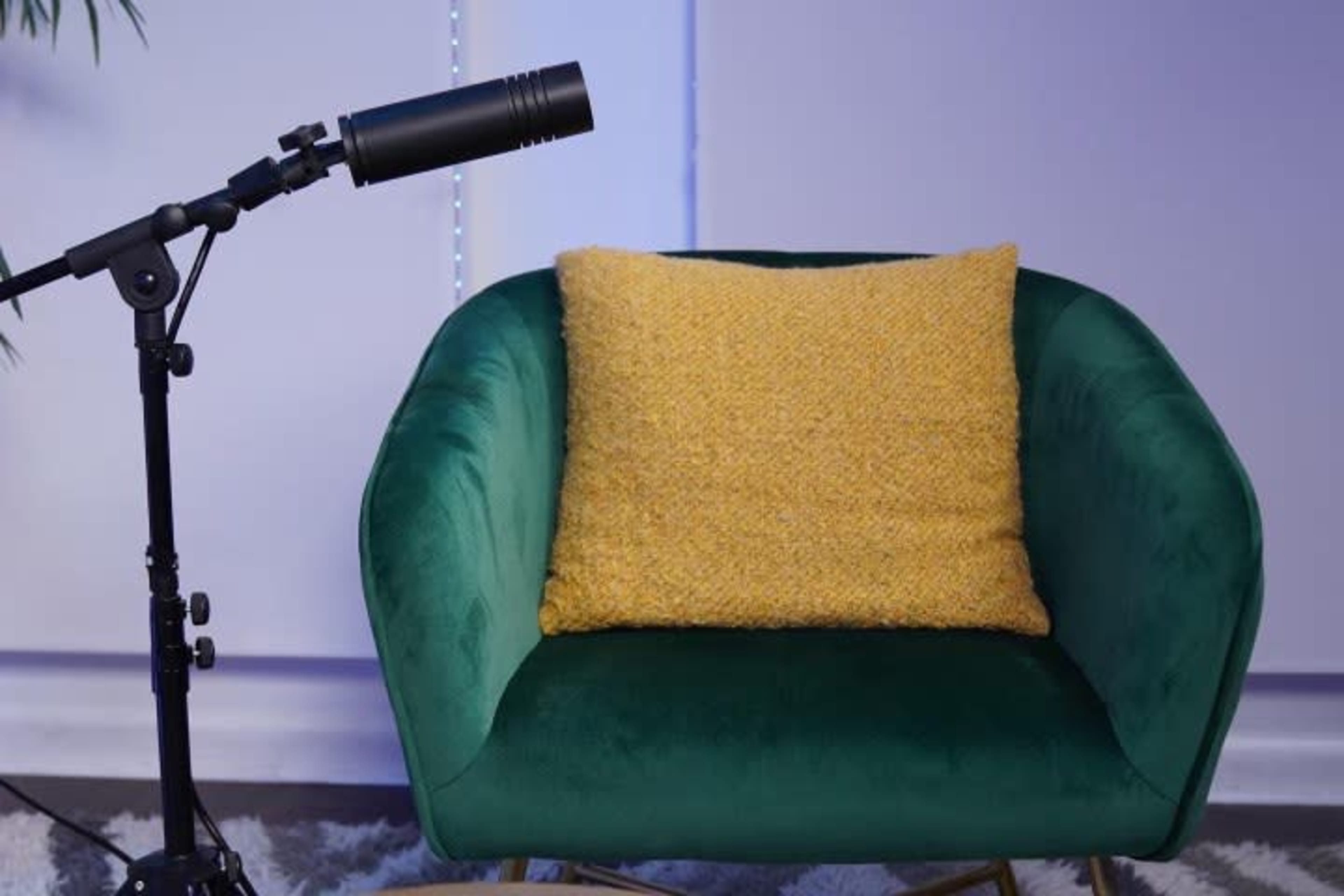 A green velvet chair with a yellow textured pillow is positioned next to a black microphone on a stand.