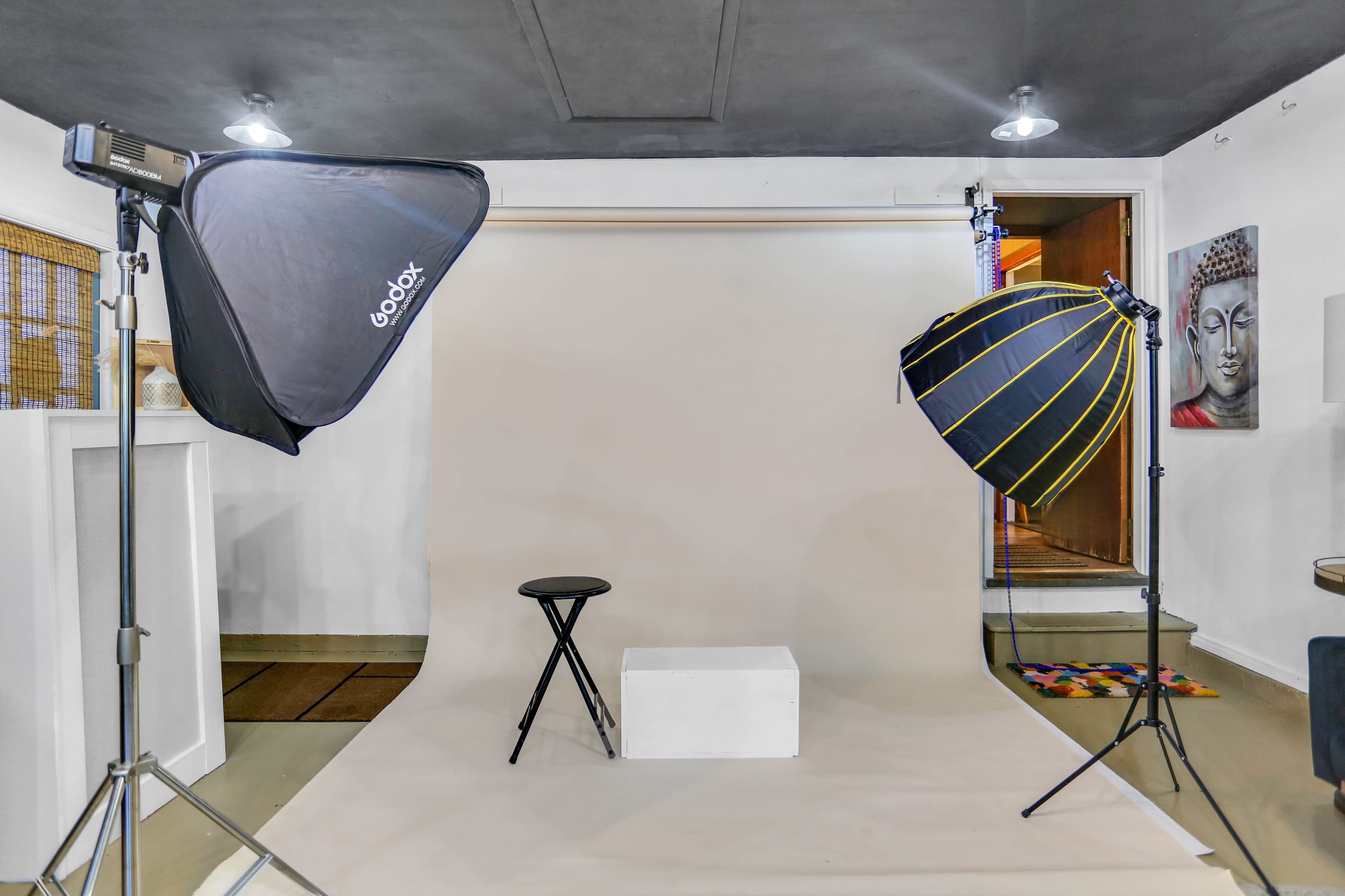 A photography studio setup featuring a plain backdrop, a stool, and two softboxes for lighting.