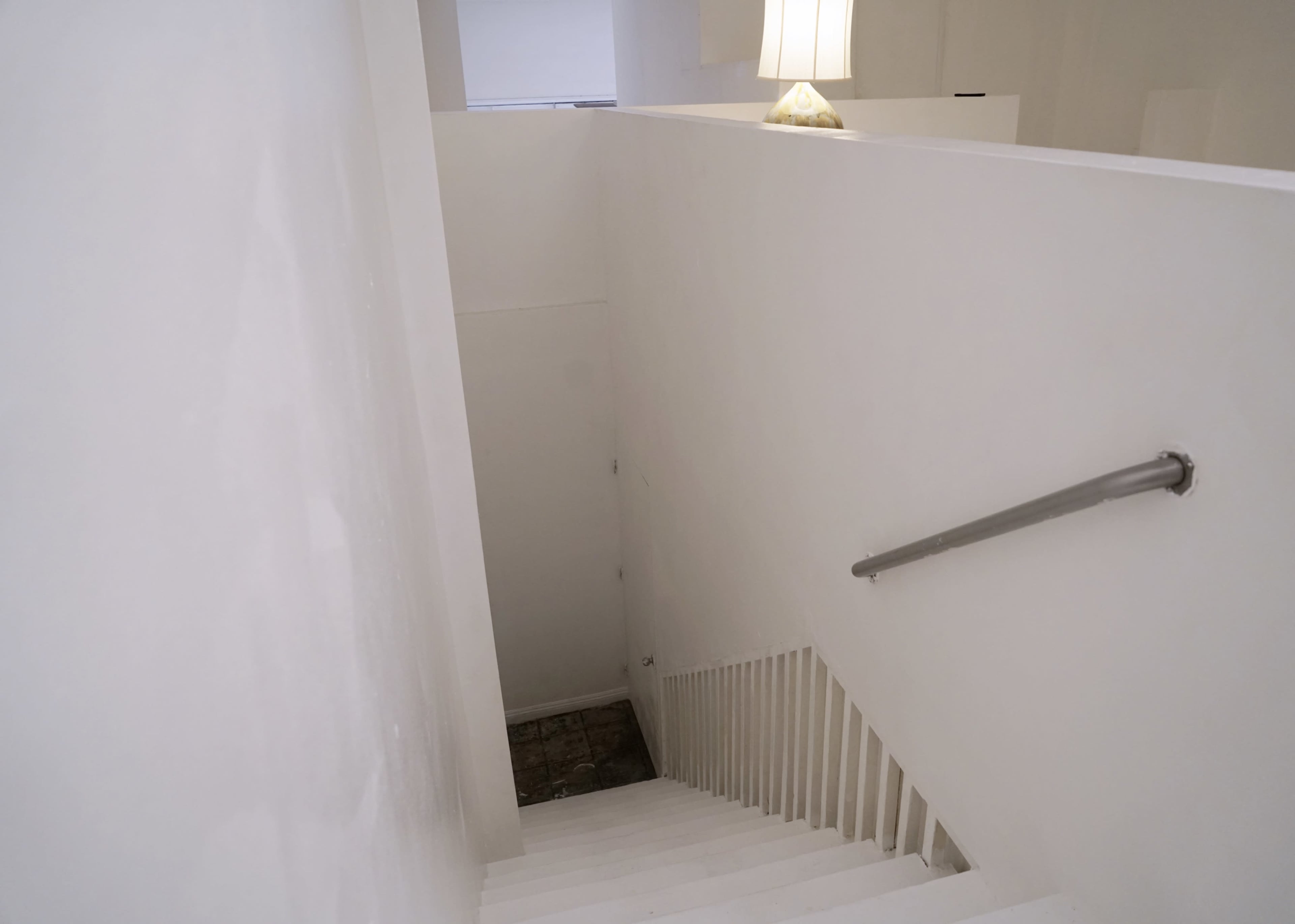 A white staircase descends into a dimly lit lower level, with a lamp casting light at the top.