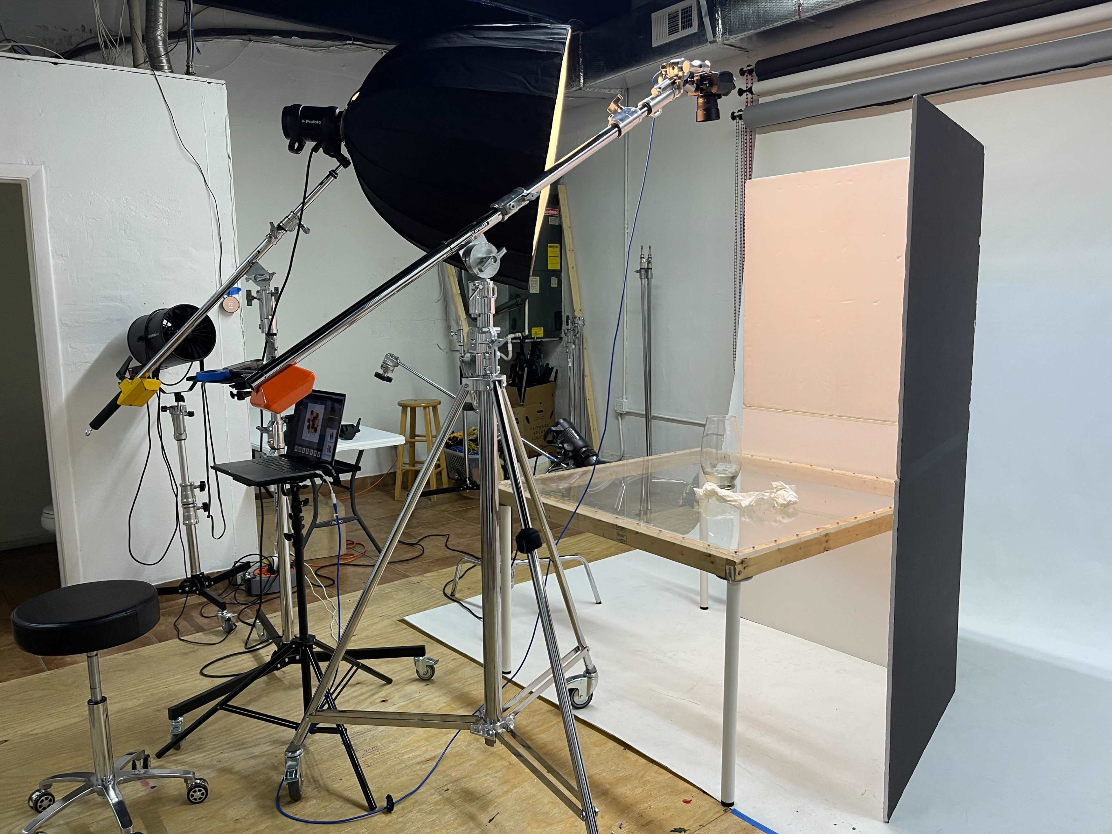 The image shows a photography studio setup with a light source on a stand, a table with a backdrop, and various equipment arranged around the space.