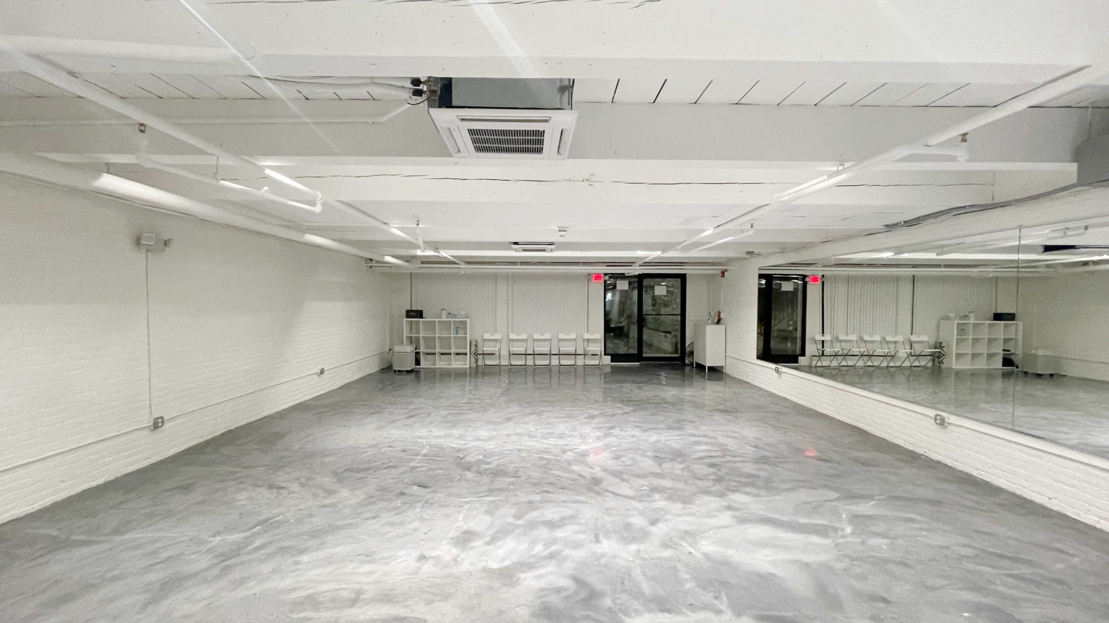 An empty, well-lit studio space with gray flooring and a large mirror on one wall.