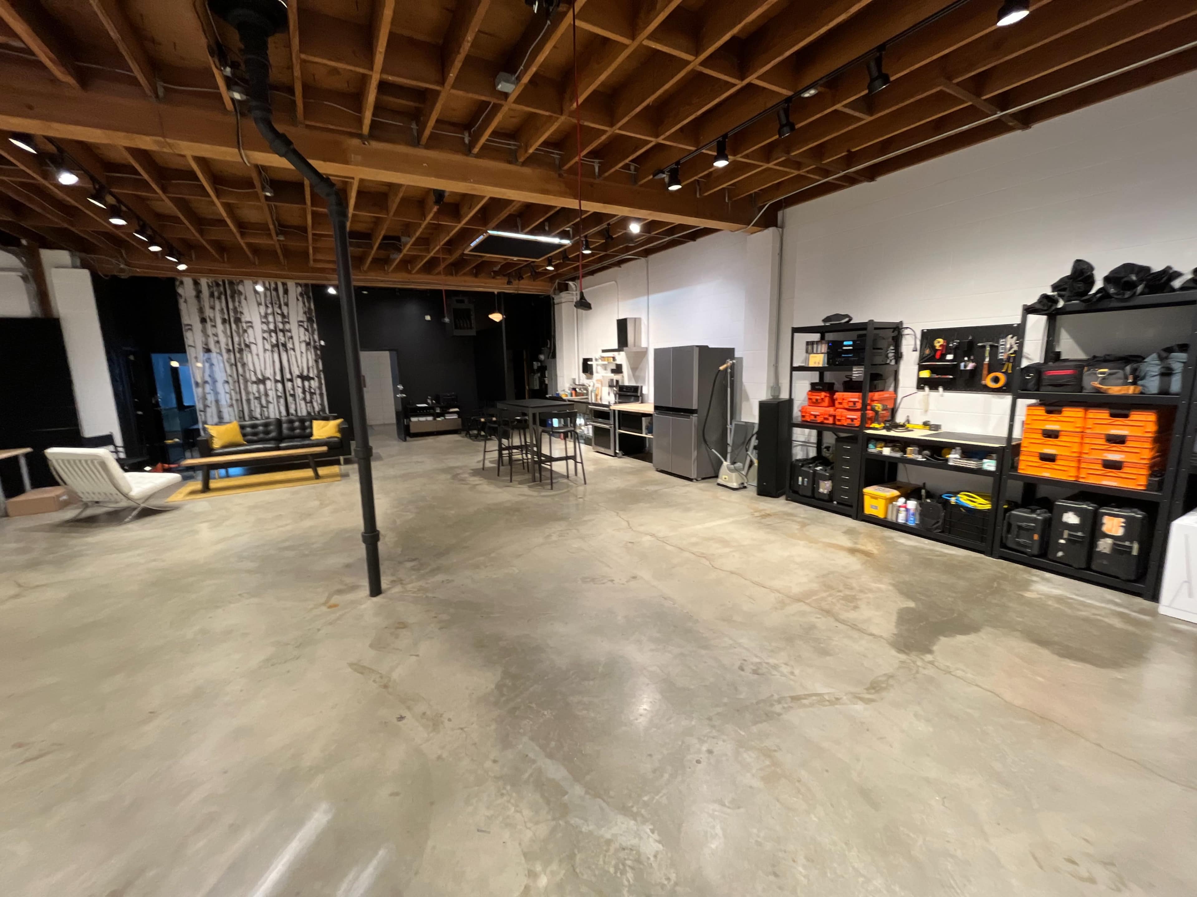 A spacious, industrial-style room with concrete floors, exposed wooden beams, and organized storage on one side.