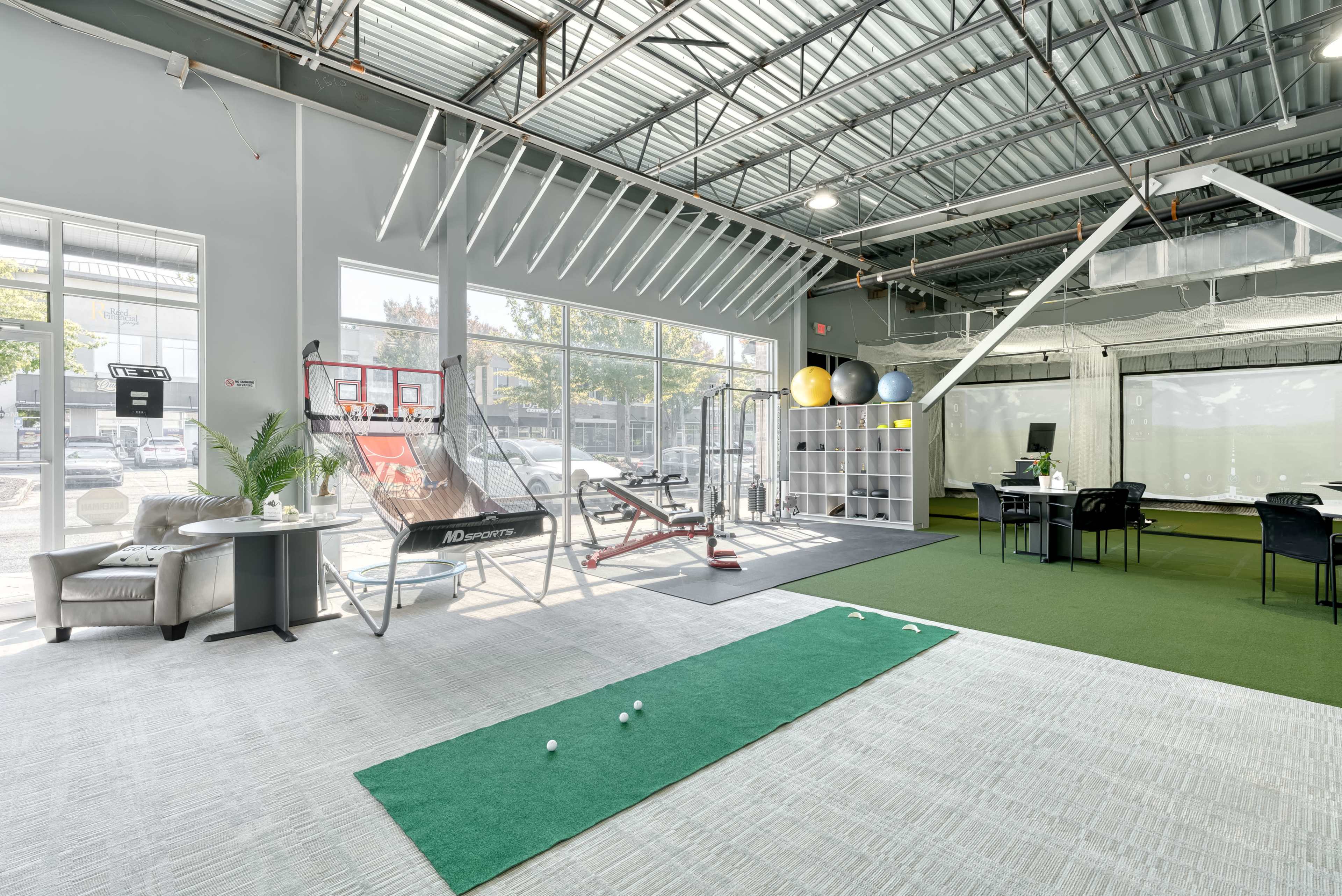 A spacious indoor training facility with a putting green, exercise equipment, and a desk area.