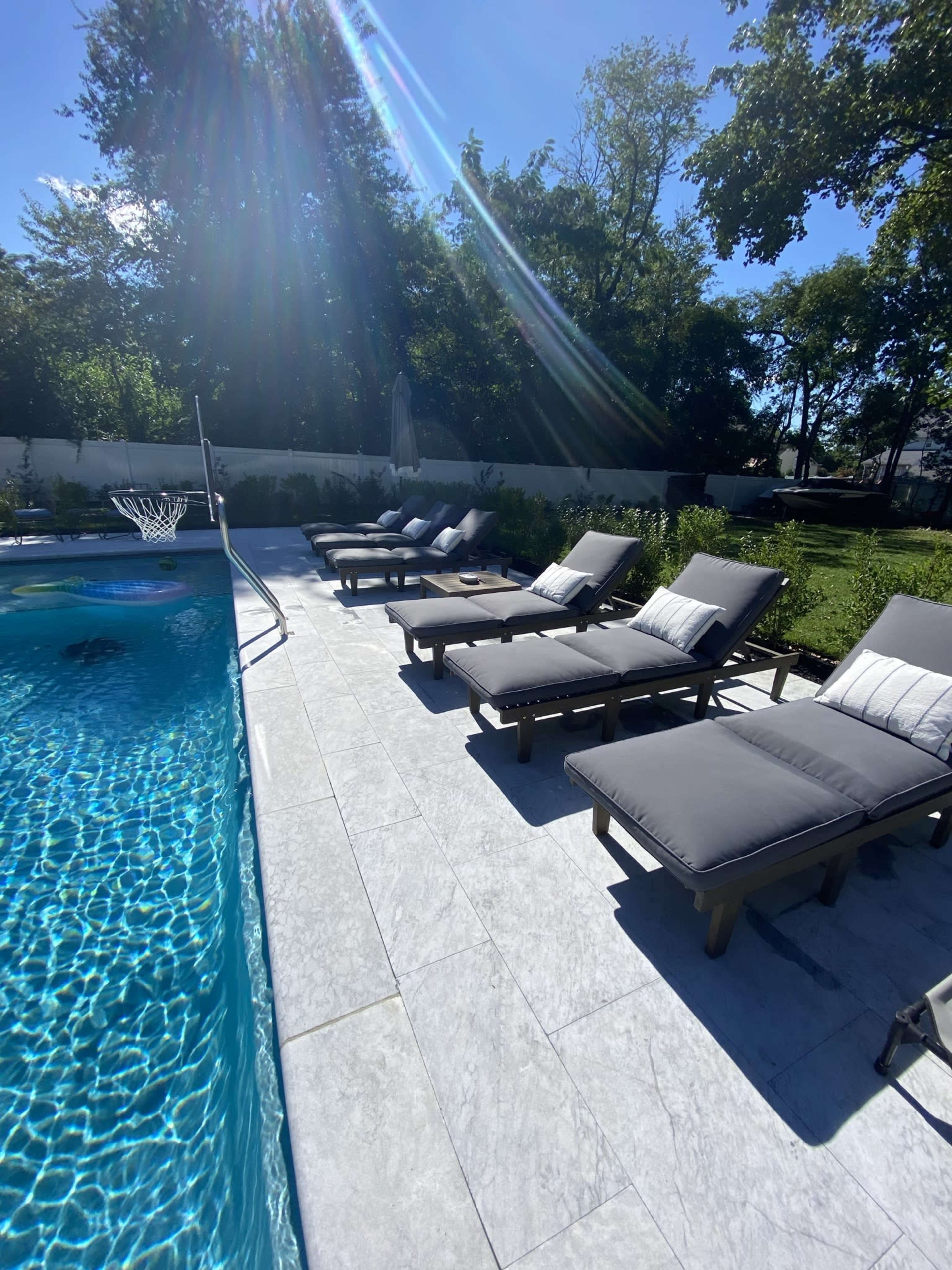 A swimming pool surrounded by several lounge chairs on a sunlit patio.